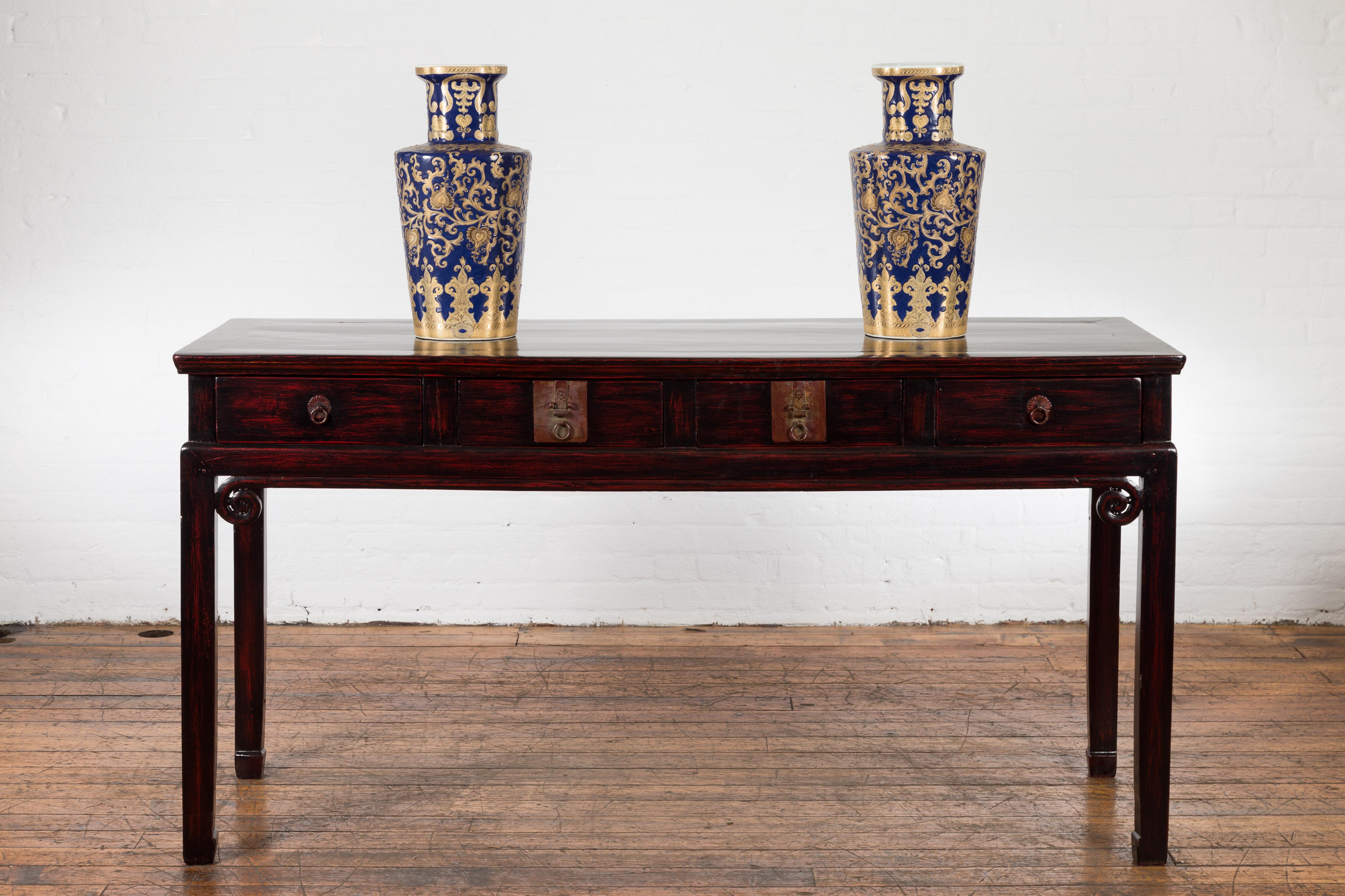 An antique Chinese late Qing Dynasty period wooden desk from the 20th century, with four drawers, carved curling scrolls, horse-hoof legs and custom black and red lacquer. Created in China during the late Qing Dynasty period in the early years of