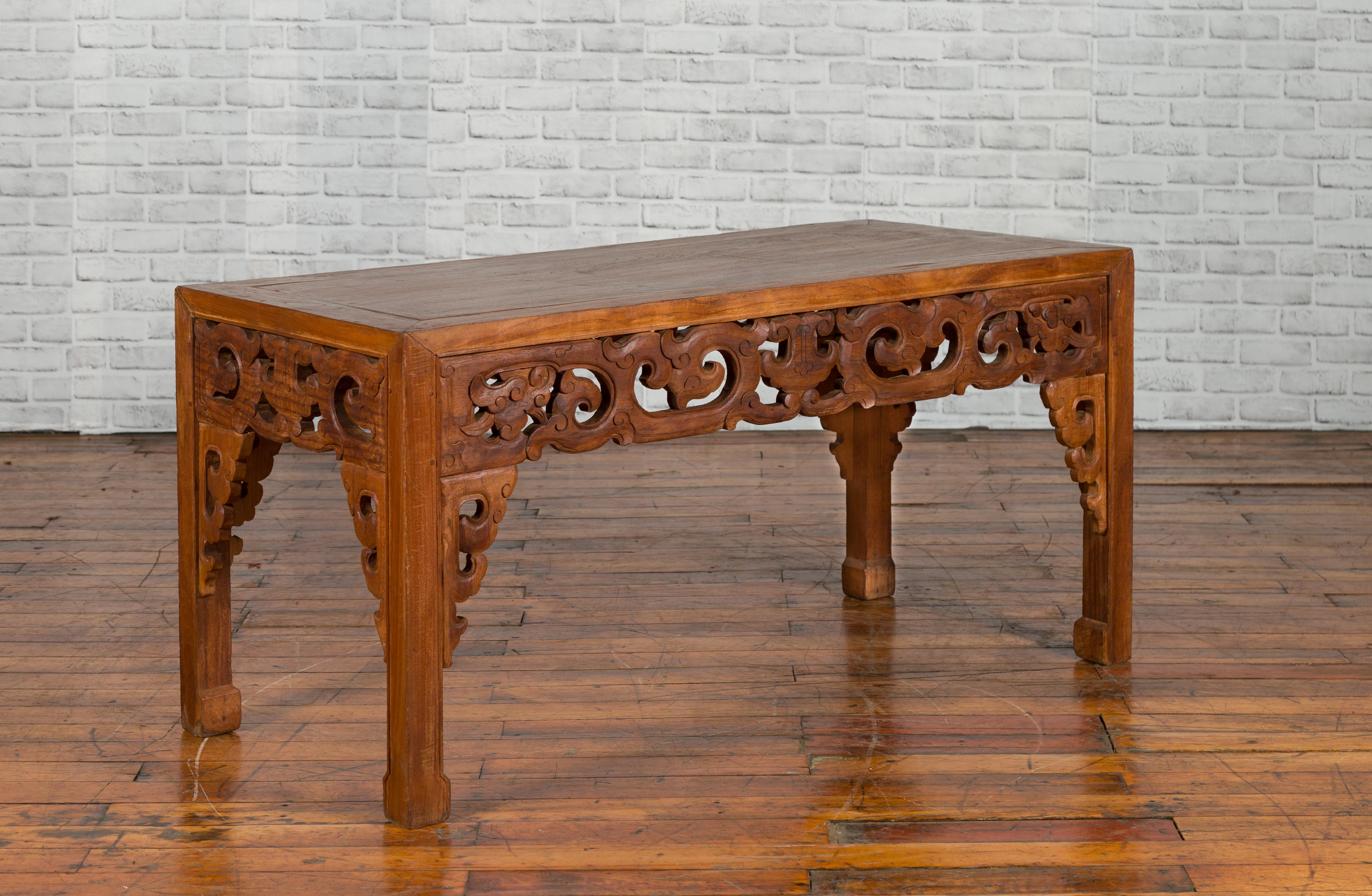 A Chinese antique low side table from the early 20th century, with cloudy carved apron. Created in China during the early years of the 20th century, this wooden side table features a rectangular top sitting above a richly carved apron depicting