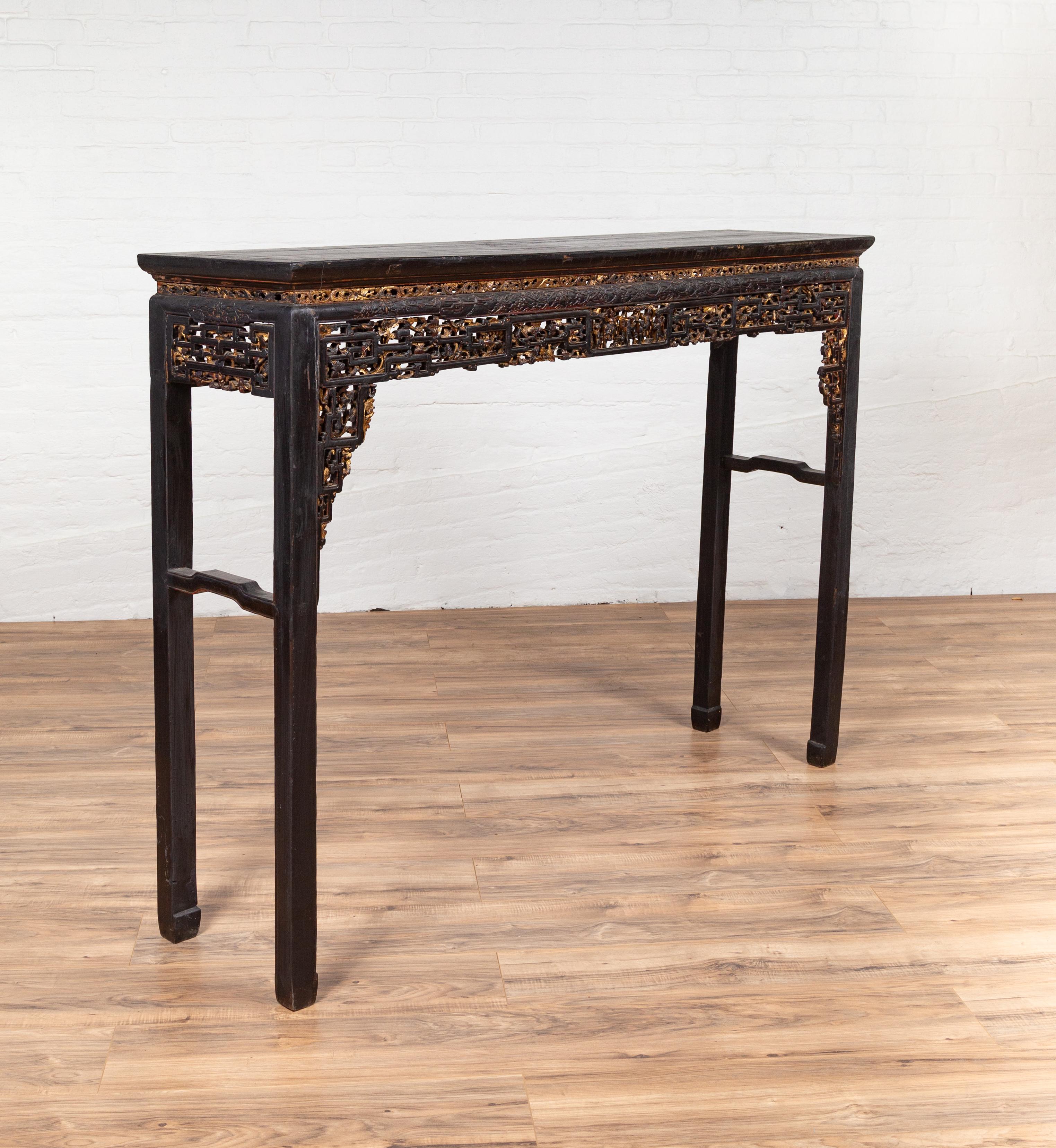 A 19th century Chinese parcel-gilt altar console table with hand carved décor, black patina and unusual size. This Chinese console table features a rectangular top sitting above a thin gilded frieze showcasing a delicate scrollwork. The apron