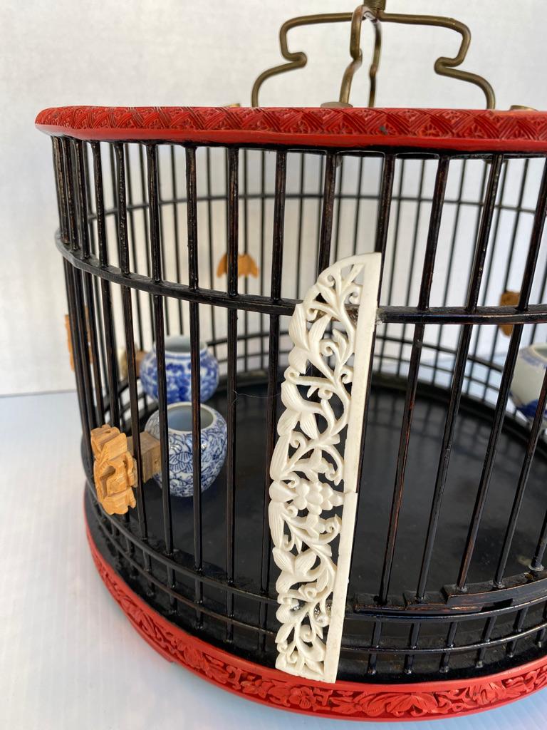 Antique black and red lacquered birdcage having hand carved accents plus little wooden pieces coral inset trim and several antique feeders of course the old hanger red lacquer surround the top and bottom area then hand carved leafy trim.