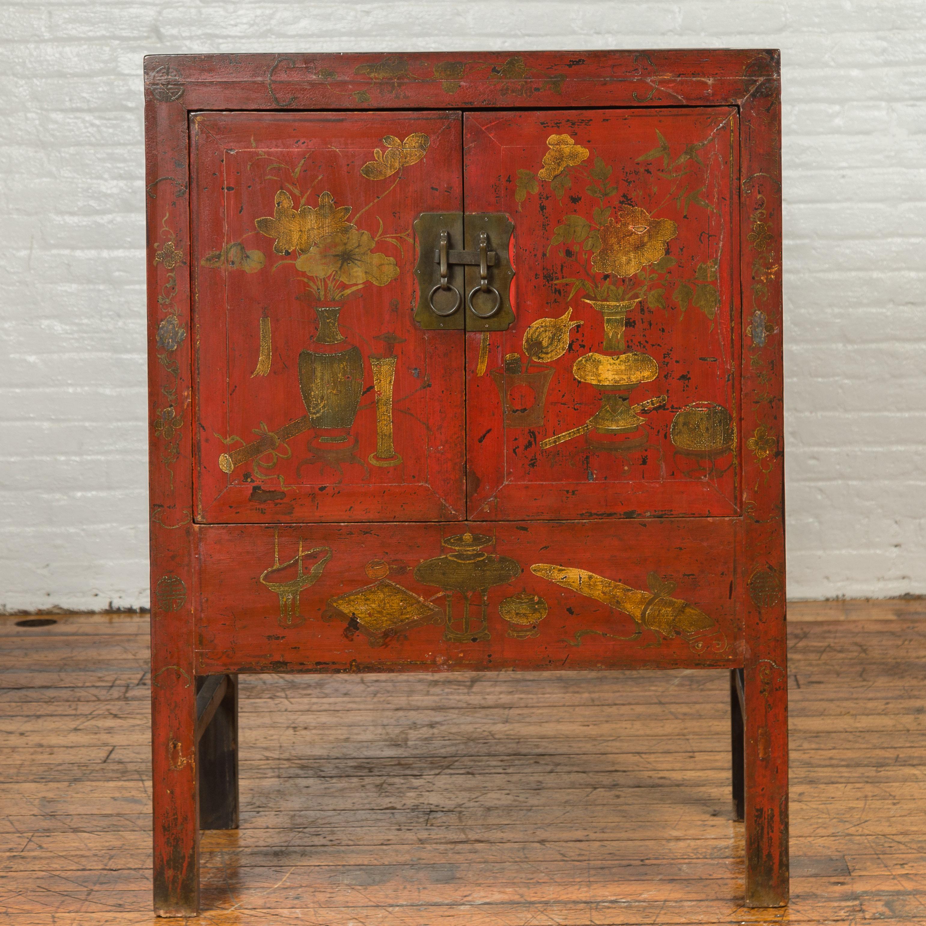 An antique Chinese red lacquered armoire from the 19th century with distressed gold floral motifs. Presenting a linear silhouette, this Chinese cabinet features a red lacquered façade delicately accented with distressed gold vases with bouquets of