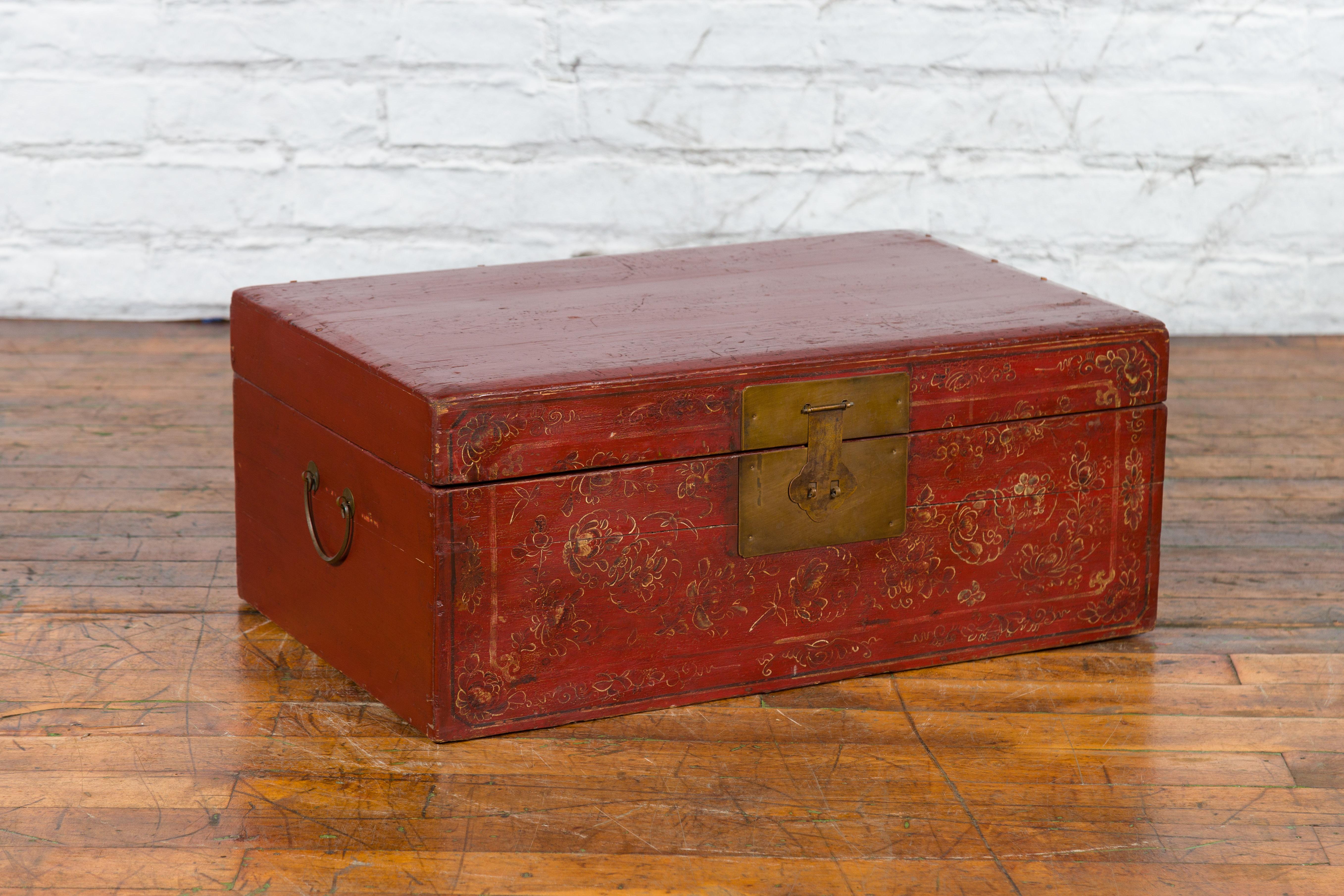 An antique Chinese red lacquered trunk from the early 20th century, with hand-painted floral décor, brass hardware, and natural interior. Created in China during the early years of the 20th century, this trunk features a linear silhouette perfectly