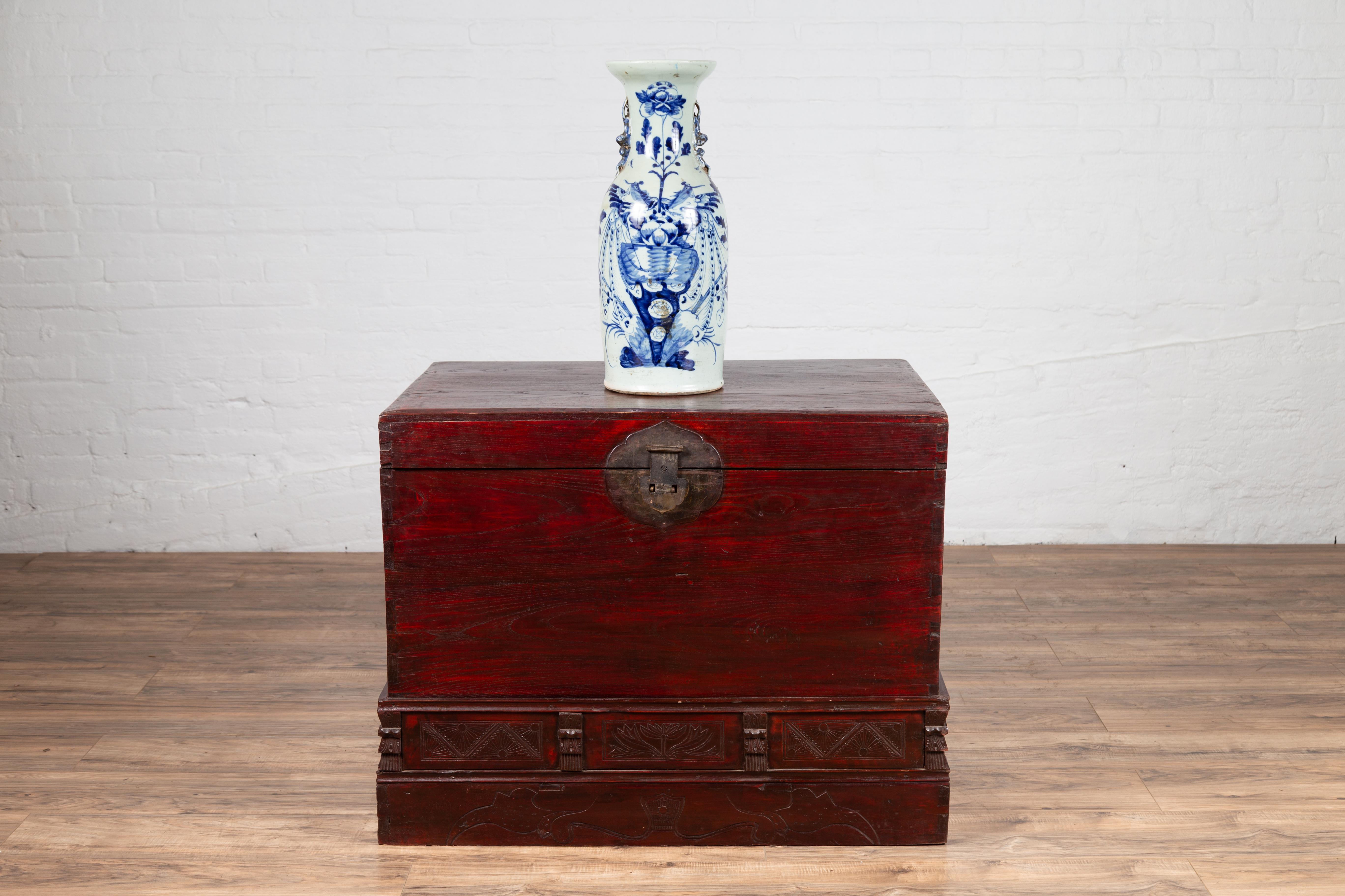 An antique Chinese red lacquered trunk from the early 20th century, with incised and carved motifs. Born in China during the early years of the 20th century, this handsome trunk boast a deep red color that captures our eyes immediately. Presenting a