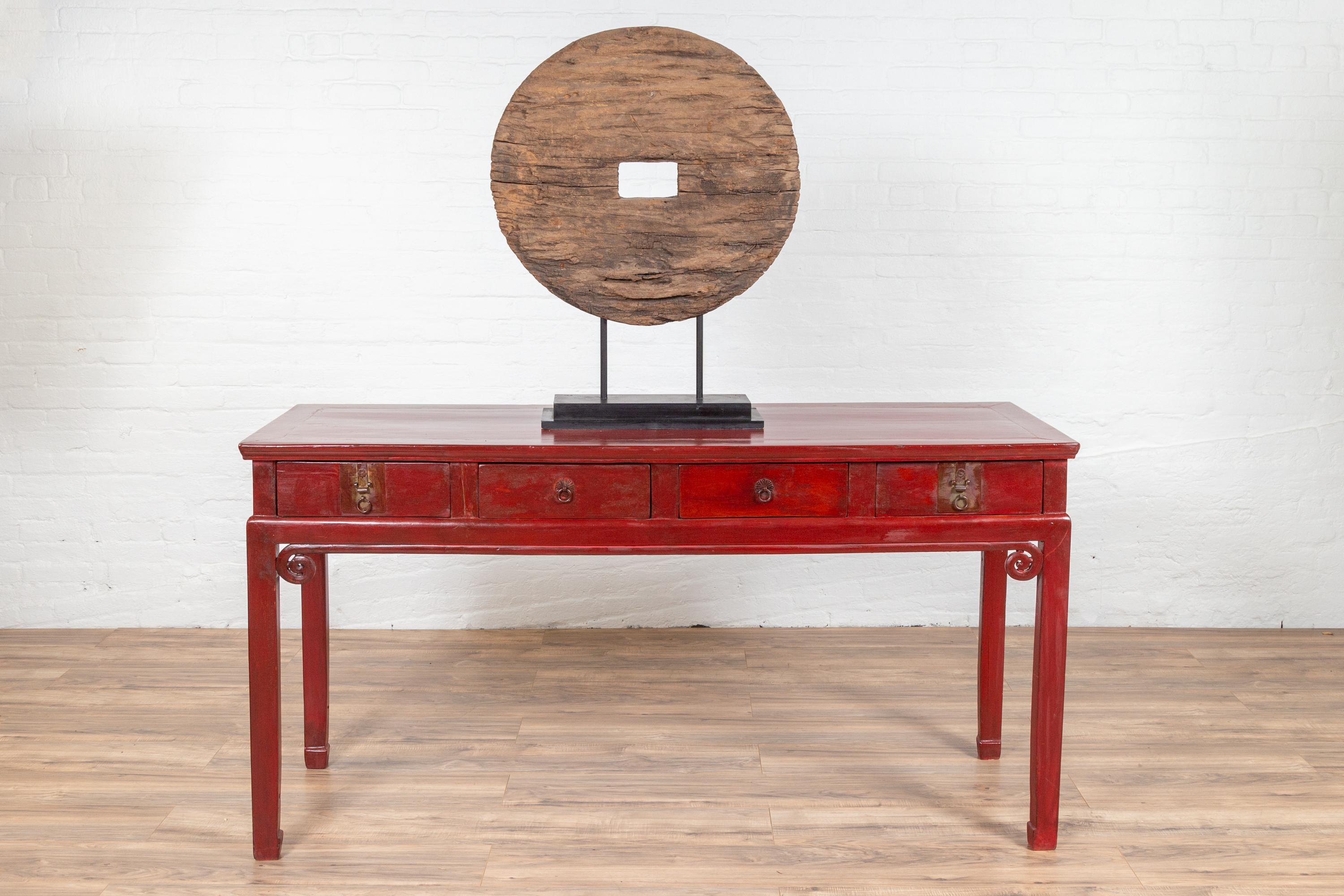 An antique Chinese red lacquer desk from the 20th century, with four drawers, curling scrolls and horse-hoof legs. Born in China in the years of the 20th century, this elegant desk grabs our attention with its deep red lacquered finish. Presenting a