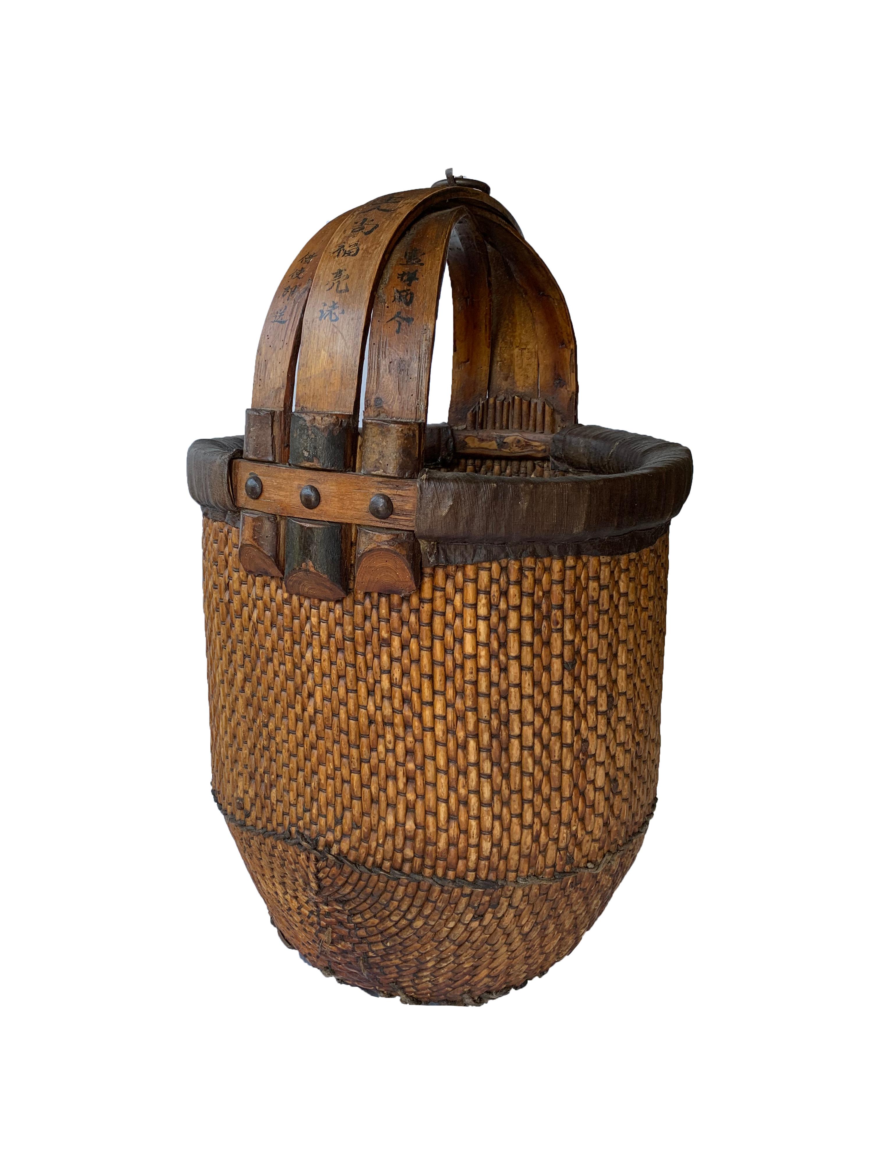 This early 20th century Chinese rice basket is handmade of tightly woven willow, lacquered and features a handle made from bent bamboo. The handle is marked with hand-painted Chinese characters on both sides. There is also a metal ring which would