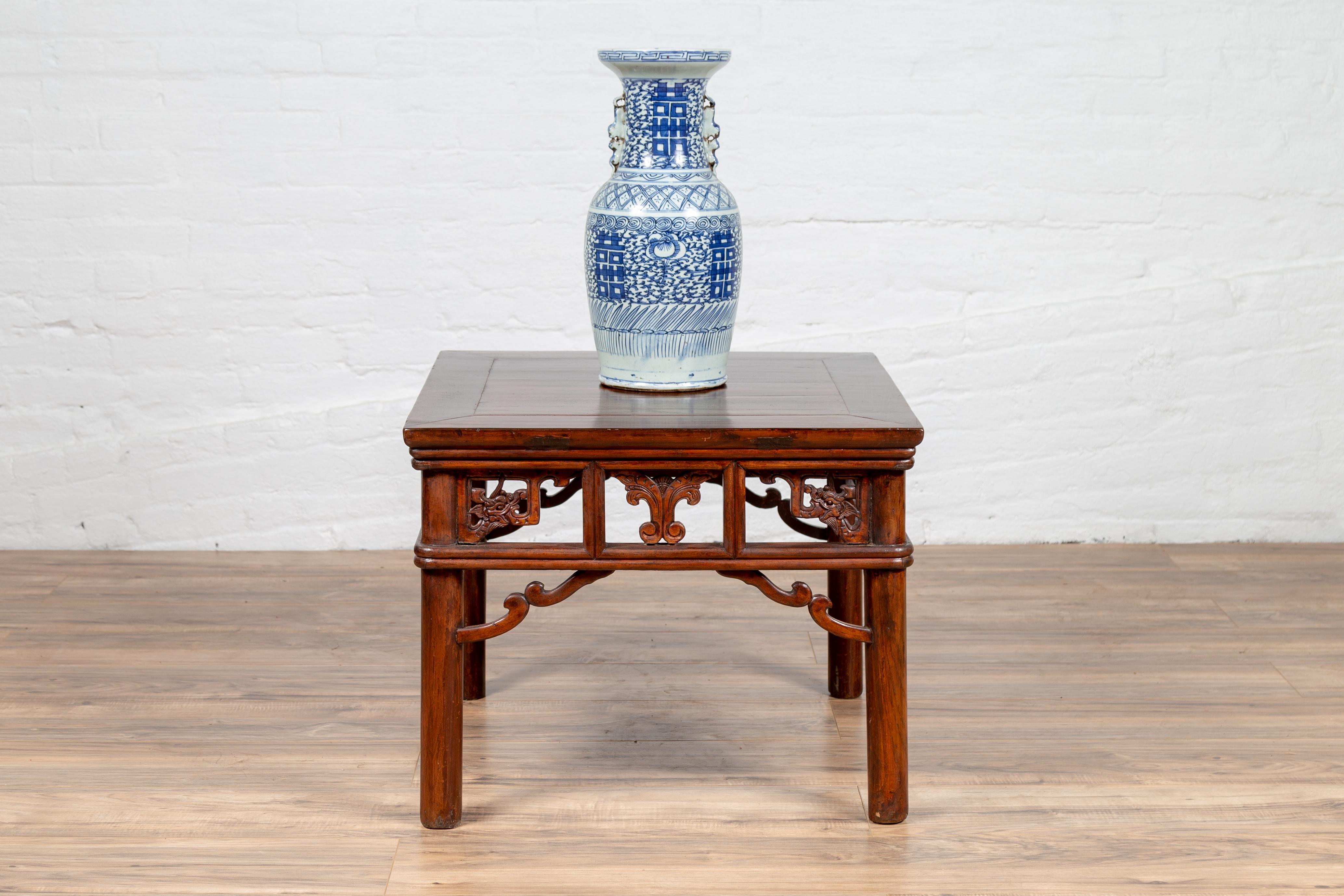 An antique Chinese Qing Dynasty period side table from the 19th century, with open fretwork design, dark wood patina and cylindrical legs. This exquisite Chinese side table features a rectangular planked top, sitting above a graceful apron. The open