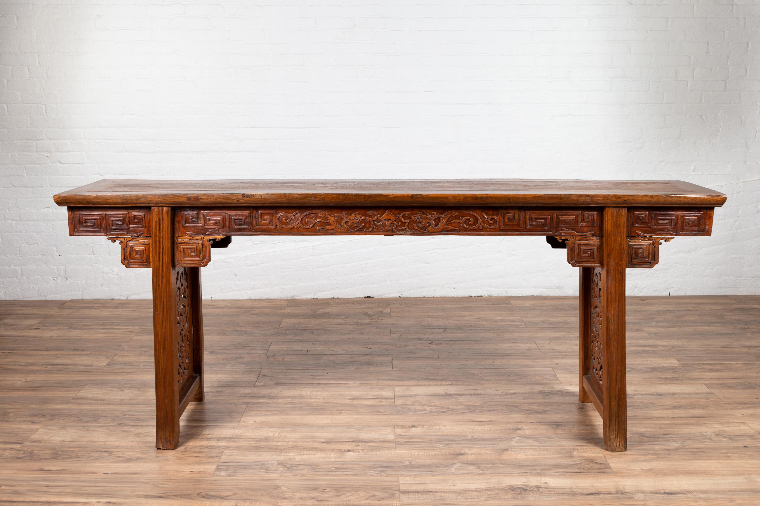 An antique Chinese tall altar console table from the early 20th century with scrollwork and pierced motifs. Born in China during the early years of the 20th century, this stunning console table charms us with its exquisitely carved decor. Featuring