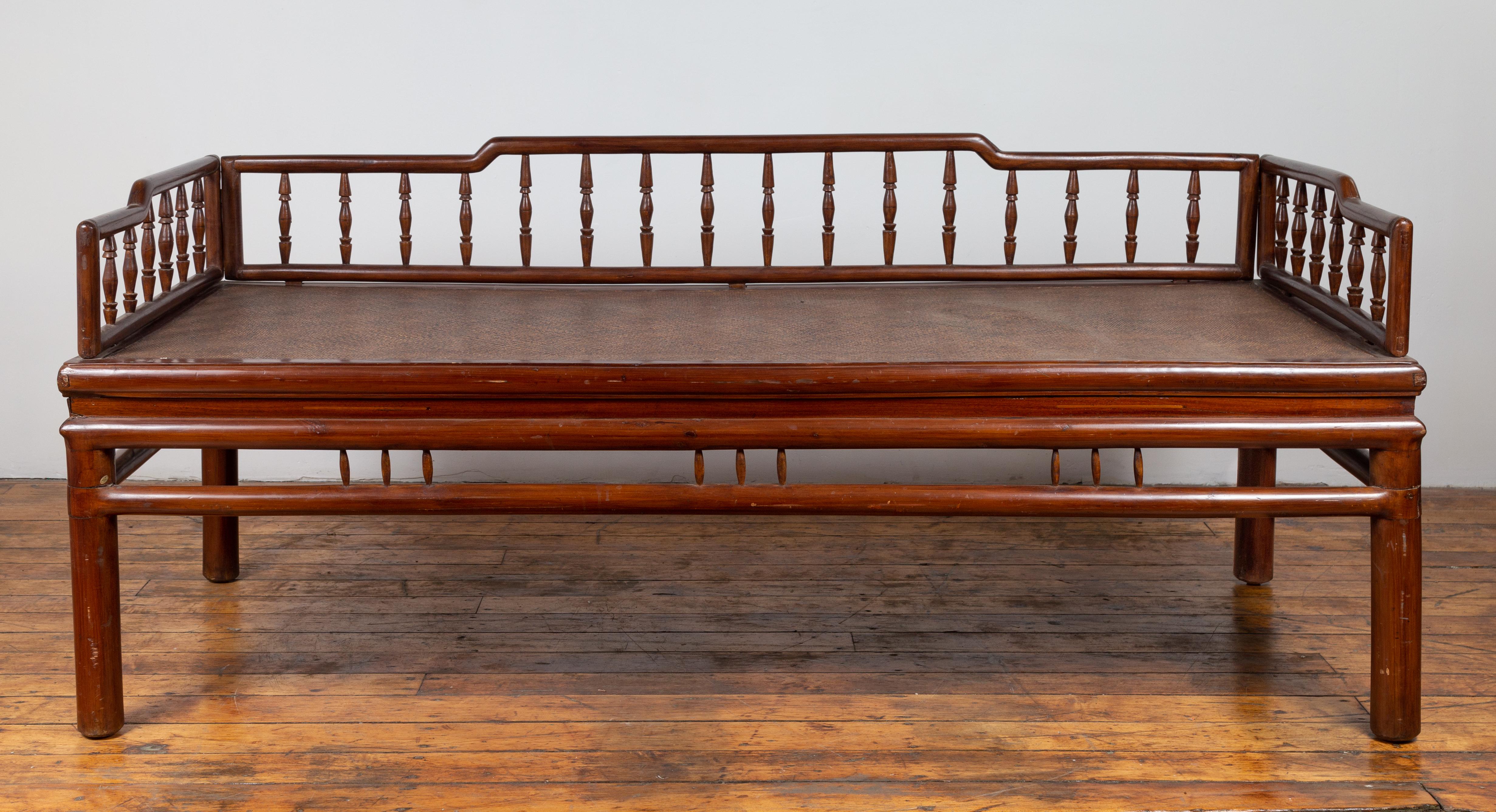 An antique Chinese wooden daybed from the early 20th century, with woven rattan seat and spindle accents. Born in China during the early years of the 20th century, this charming daybed features a pierced back with spindle motifs and humpbacked rail.