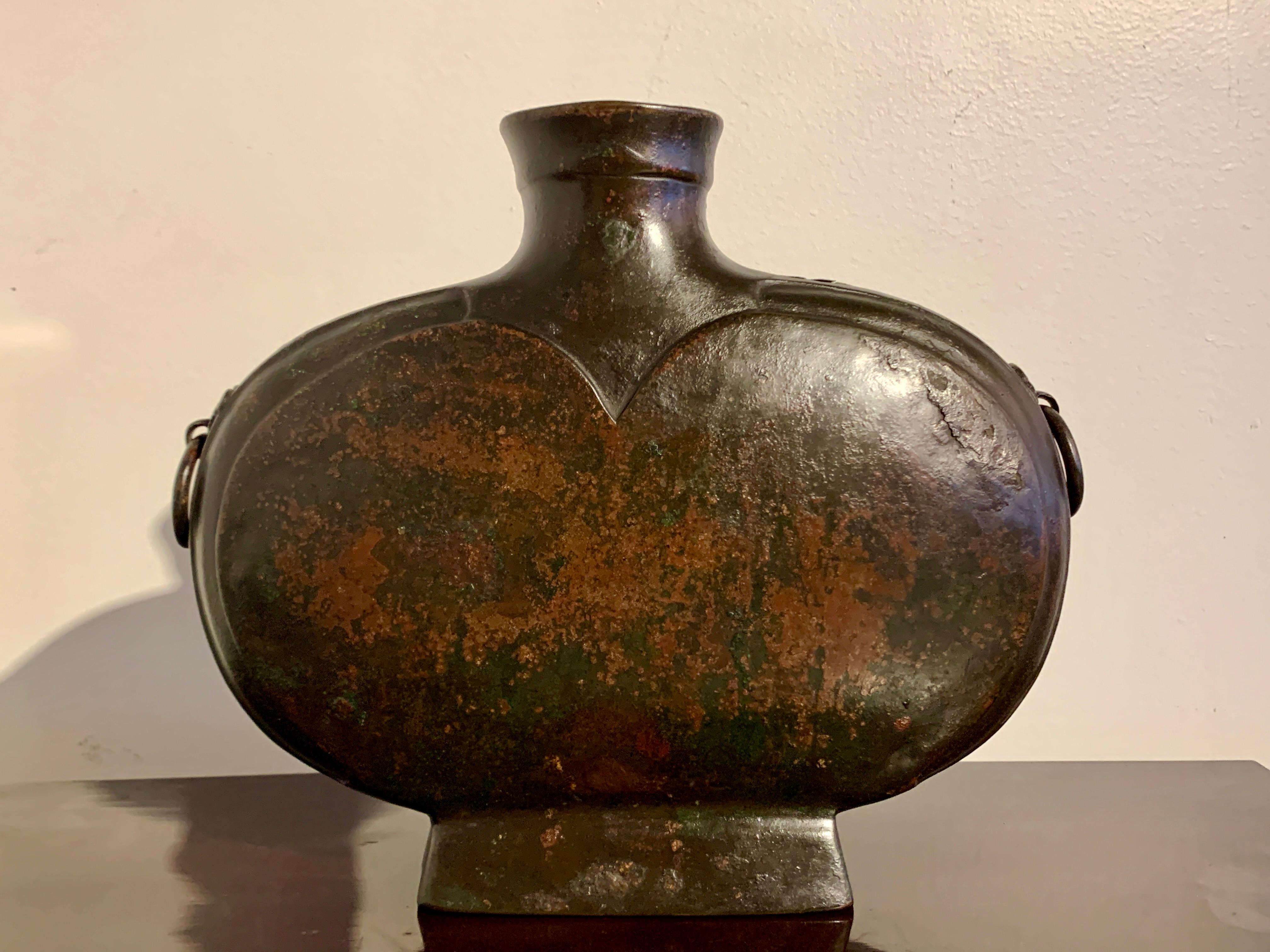 A sublime Chinese archaic bronze wine vessel, called a bianhu, Han Dynasty (206 BC - 220 AD), China.

The bianhu with a flattened oblong body, applied taotie masks, and loose ring handles. The bronze wine vessel set on a high rectangular splayed