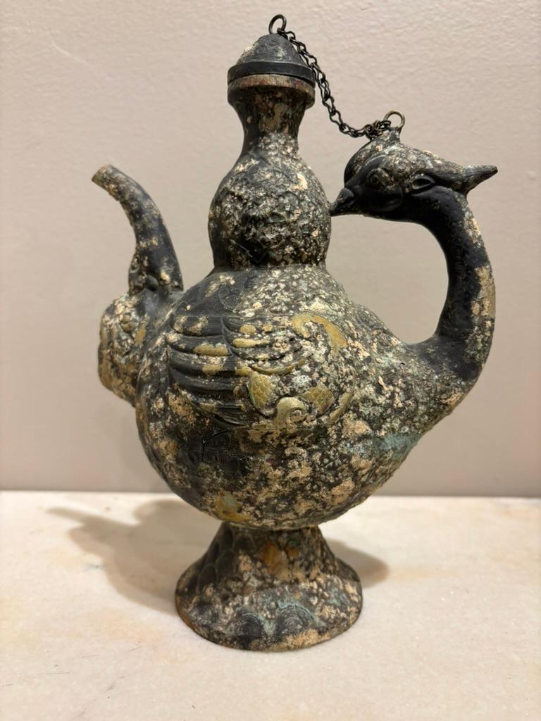 Vaso rituale arcaico cinese in rame repousse con beccuccio a testa di ariete e manico e corpo a forma di uccello fenice. Un pezzo splendidamente realizzato in stile antico con dettagli intricati. Le ali della fenice avvolgono il corpo, con un