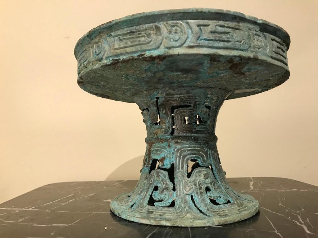 A Chinese bronze bowl on stand in the form of a tazza with wonderful verdigris patina. Warring States style (2-3rd century BC). The dish top bordered with incised decoration, the base with openwork and incised archaistic designs.