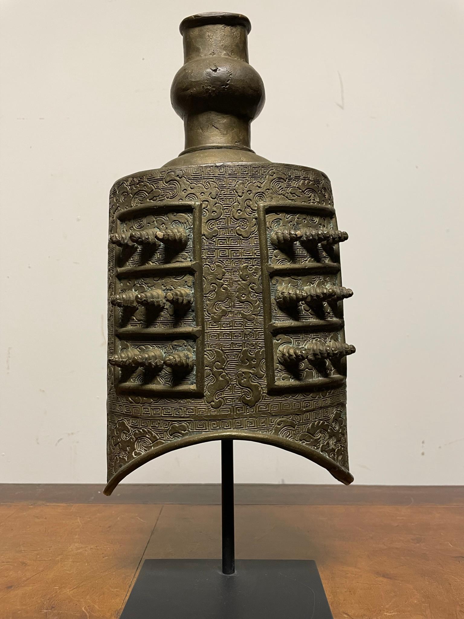 
A Chinese bronze bell, or Zhong, in the style of the Zhou dynasty (770-256 B.C.) Circa 1900. 
Cast in two lenticular sections, each side divided in half and decorated with alternating rows of three raised cylindrical bosses within sectioned