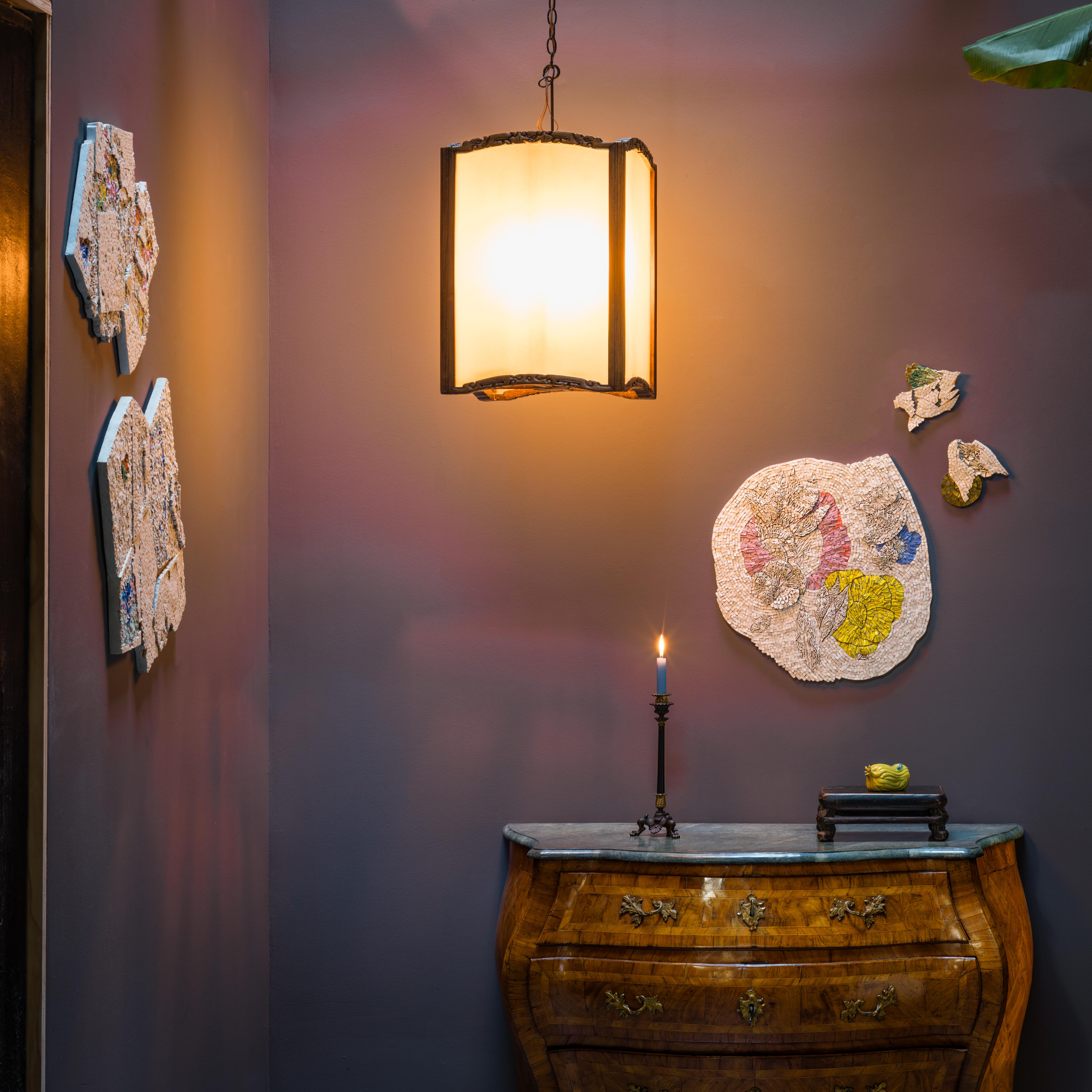 Framed in hand-carved rosewood, this 19th-century hanging lantern casts a soft glow through frosted glass. The lantern has a square frame, with straight sides and gently arched tops carved with abstract dragons and bats, symbols of strength and