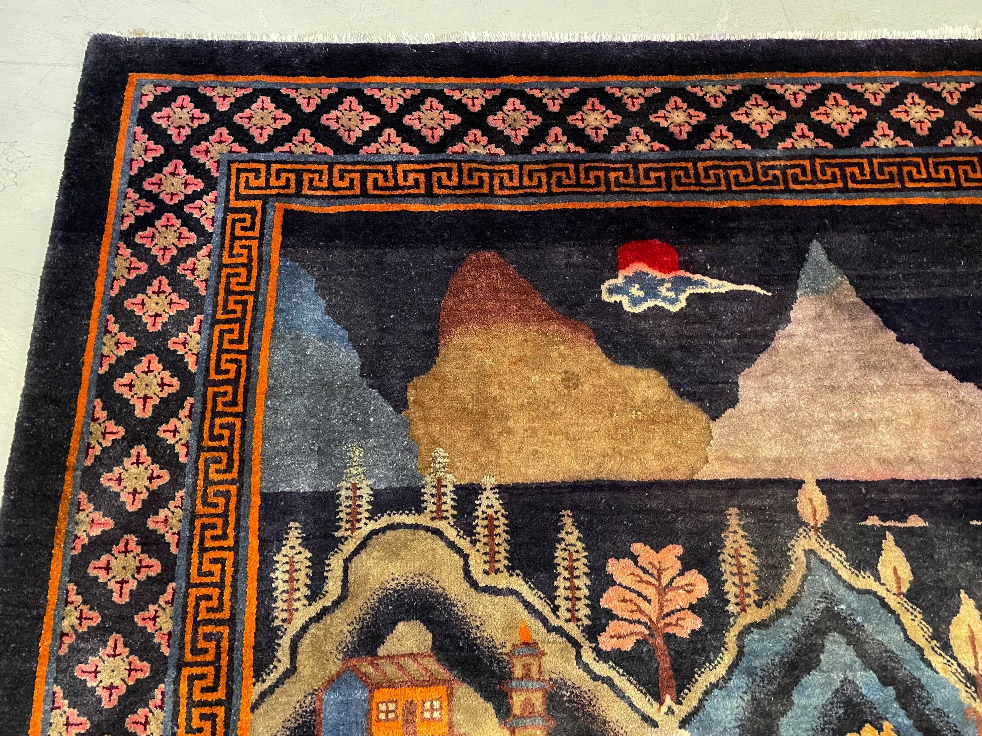 A Chinese Art Deco pictorial landscape wool rug from Baotou in the Inner Mongolia region. Beautifully scenic view of a village on a lake surrounded by mountains with trees, houses, a pagoda and a bridge or aqueduct. Rich saturated color, the main