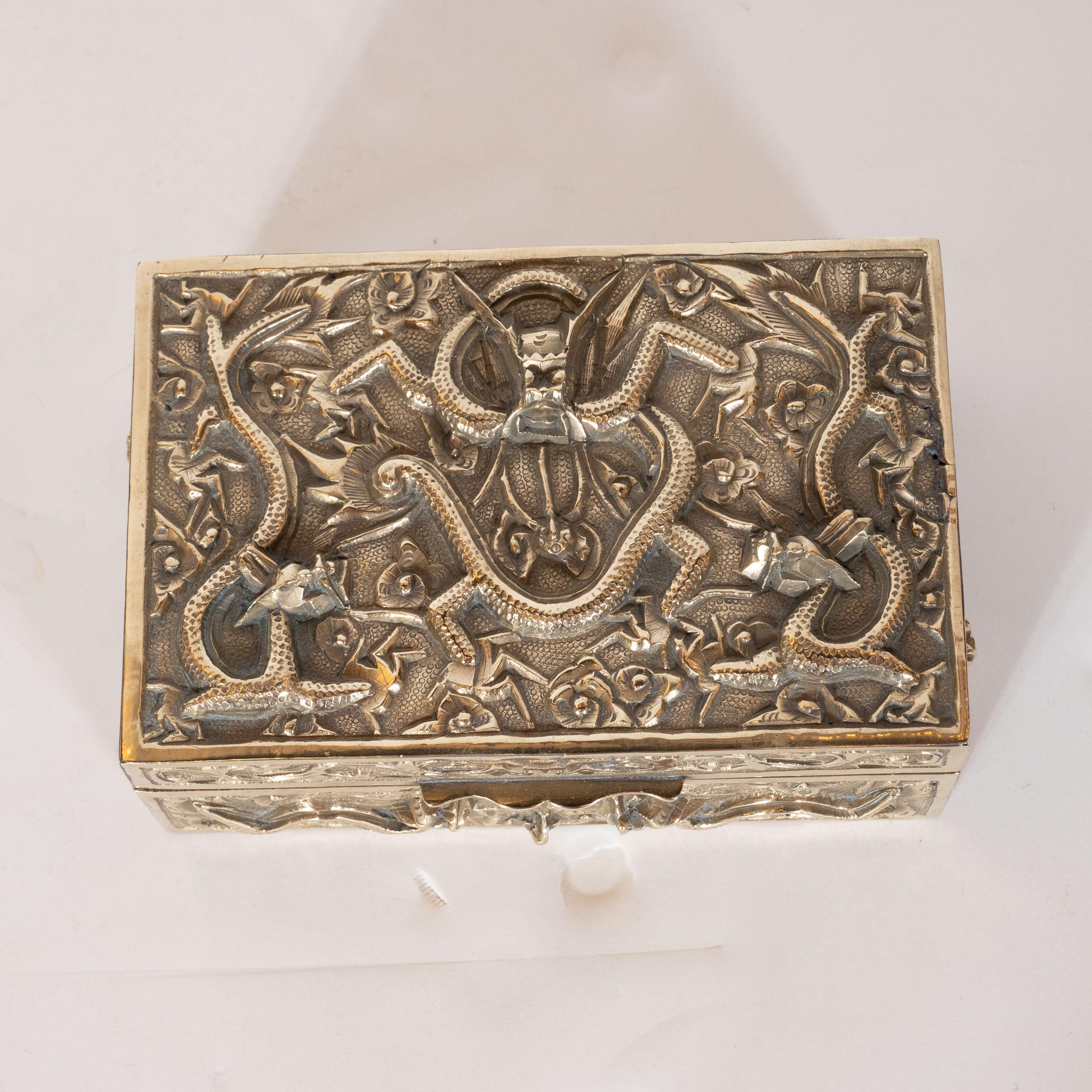 This stunning decorative box was realized in China, circa 1930. It features a rectangular body with a stippled texture and undulating dragons, as well as stylized floral/foliate motifs, inscribed in high relief throughout the surface of the piece.