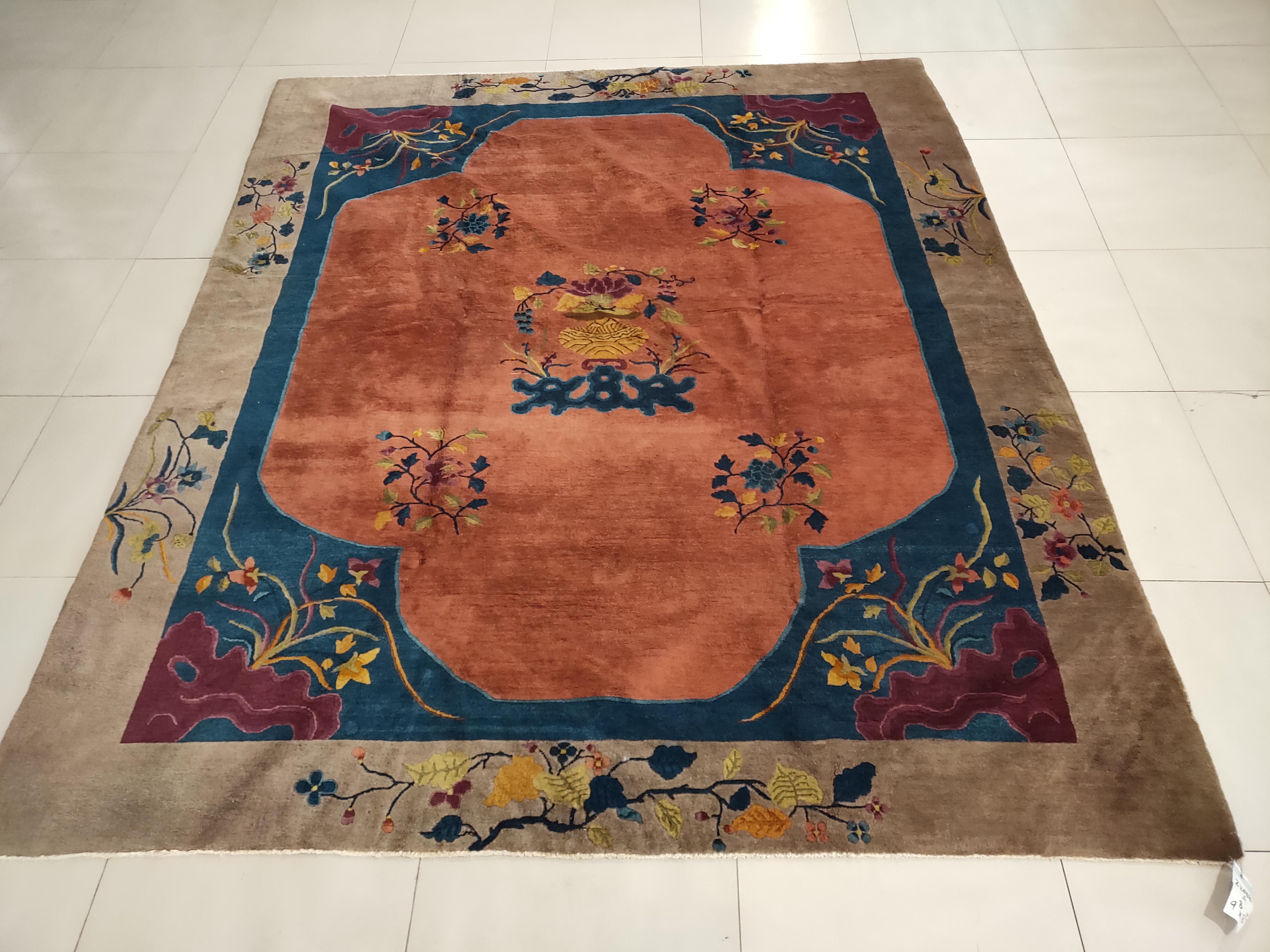 A four lobed, nearly open, apricot field is centered on a vase on stand with flowering bouquet, rocks and more flowers fill the blue corners of this 1920s Chinese carpet in the Art Deco style from Tianjin in northeast China.