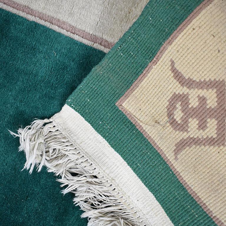 A rectangular green art deco rug with Chinese characters around the edges. A lovely piece in a beautiful emerald green around the edges and at the center. A cream border surrounds the inner edges and is decorated with Chinese characters in brown.