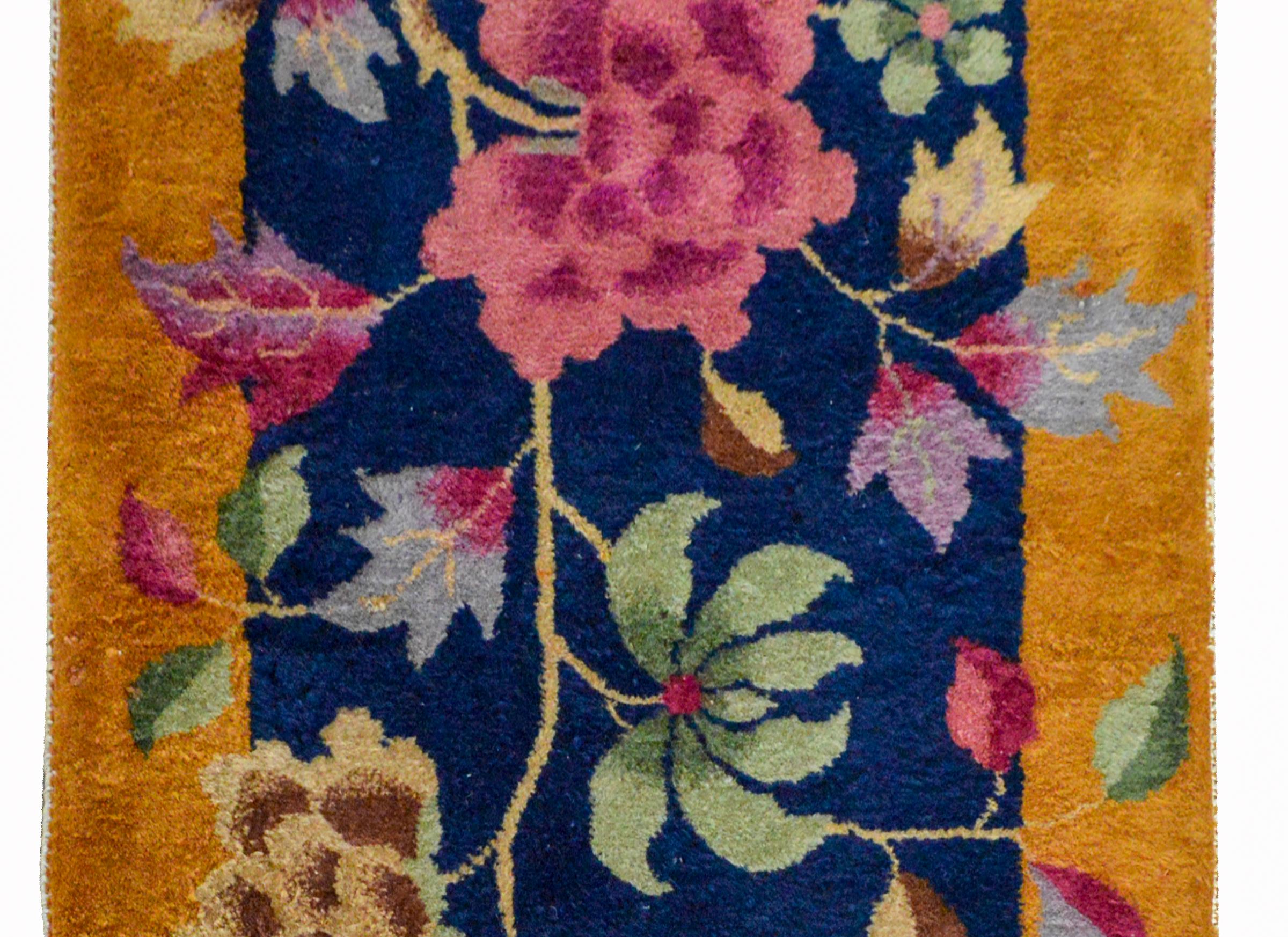 A bold early 20th century Chinese Art Deco rug with a large tree peony woven in myriad colors including pink, cream, green, indigo, and violet, against a dark indigo background and surrounded by a wide gold border.