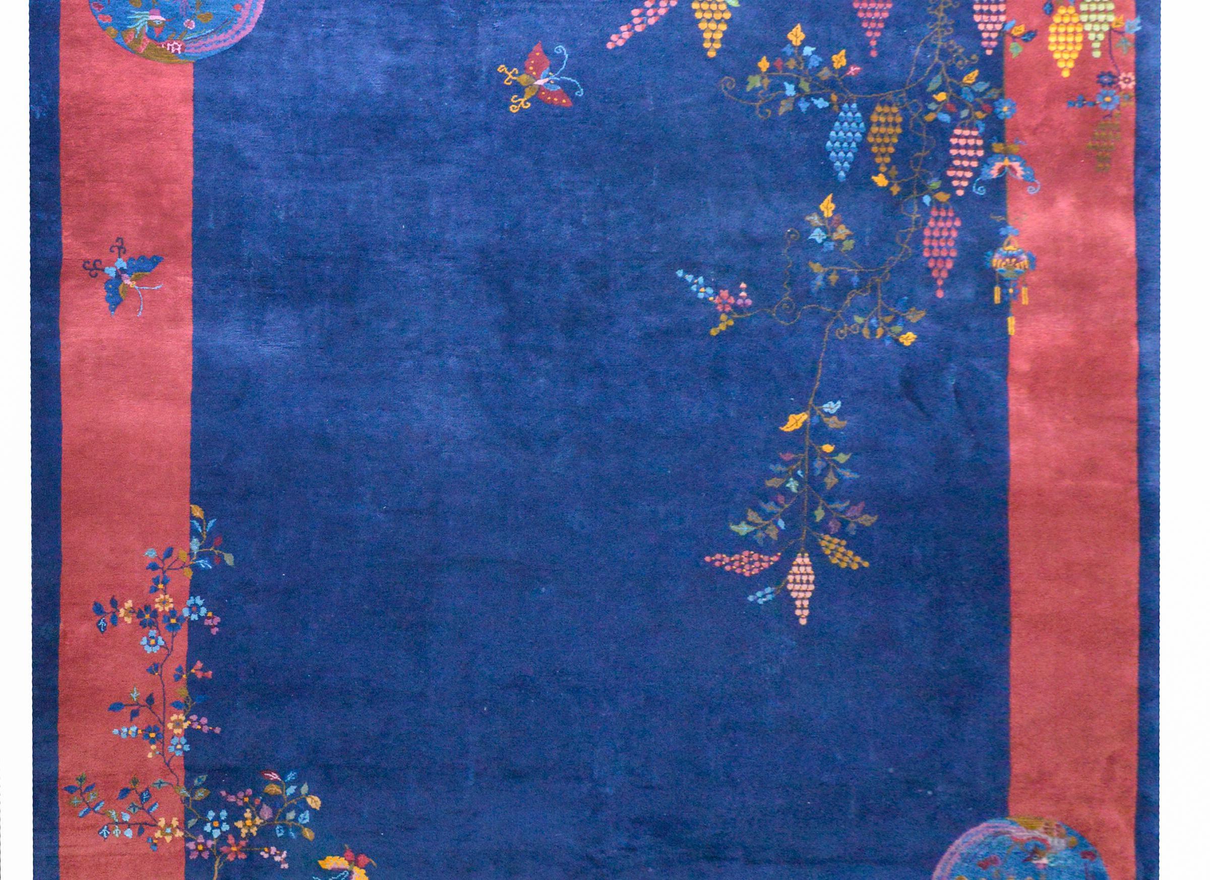 A wonderful early 20th century Chinese Art Deco rug with a dark indigo field surrounded by a wide dark cranberry and a thin indigo border. Myriad auspicious flowers including peonies, chrysanthemums, wisteria, and cherry blossoms, all woven in