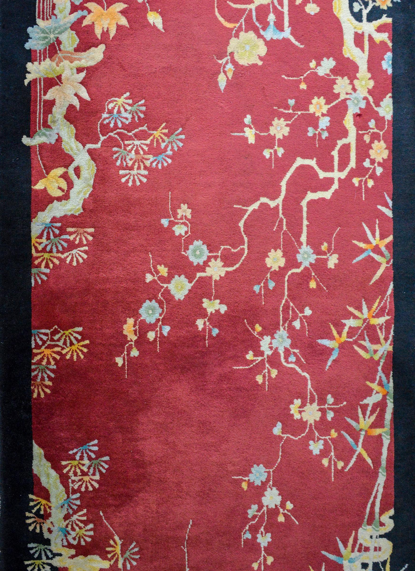 A beautiful early 20th century Chinese Art Deco rug with a deep cranberry colored background surrounded by a black border, and myriad auspicious flowers including bamboo, peonies, lotus, and cherry blossoms all woven in pale blues, oranges, yellows,