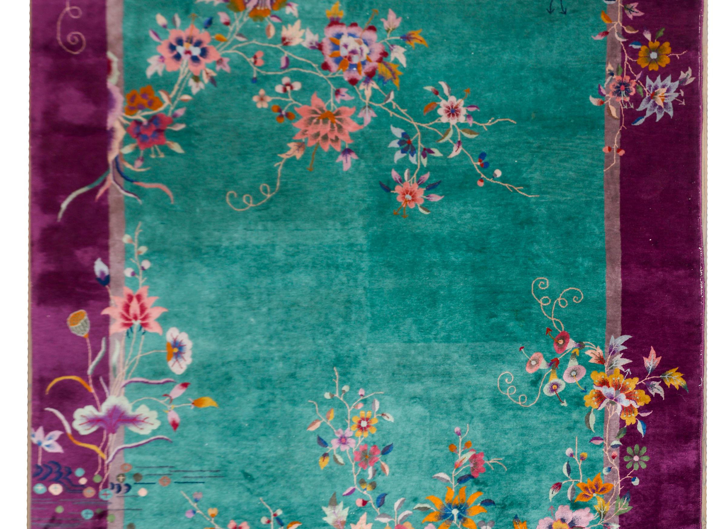 A gorgeous early 20th century Chinese Art Deco rug with a wide eggplant colored border surrounding a teal field, and bother laid with the most beautiful large-scale multi-colored peonies, lotus, and chrysanthemums.