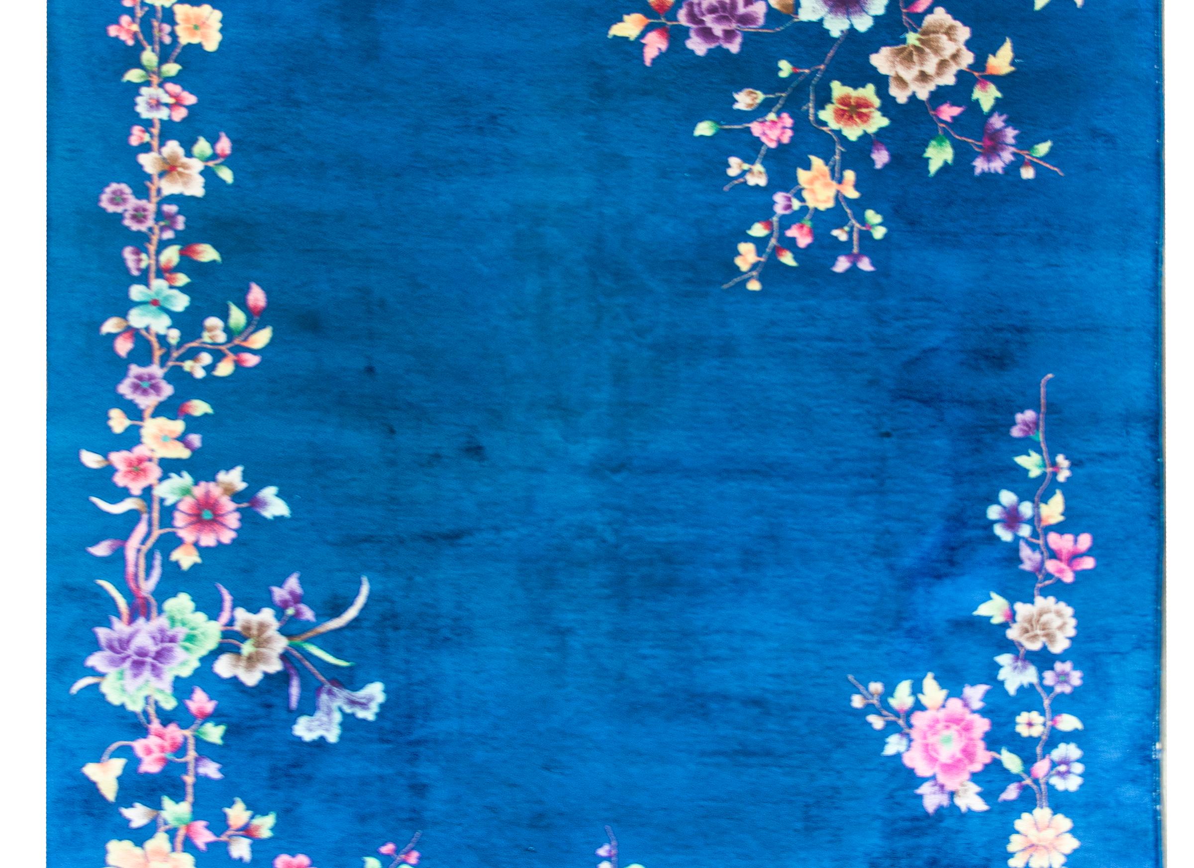 A stunning early 20th century Chinese Art Deco rug with a gorgeous cobalt blue field with an asymmetrical composition of multi-colored flowers including peonies, lotus, and chrysanthemums creating an incomplete border.