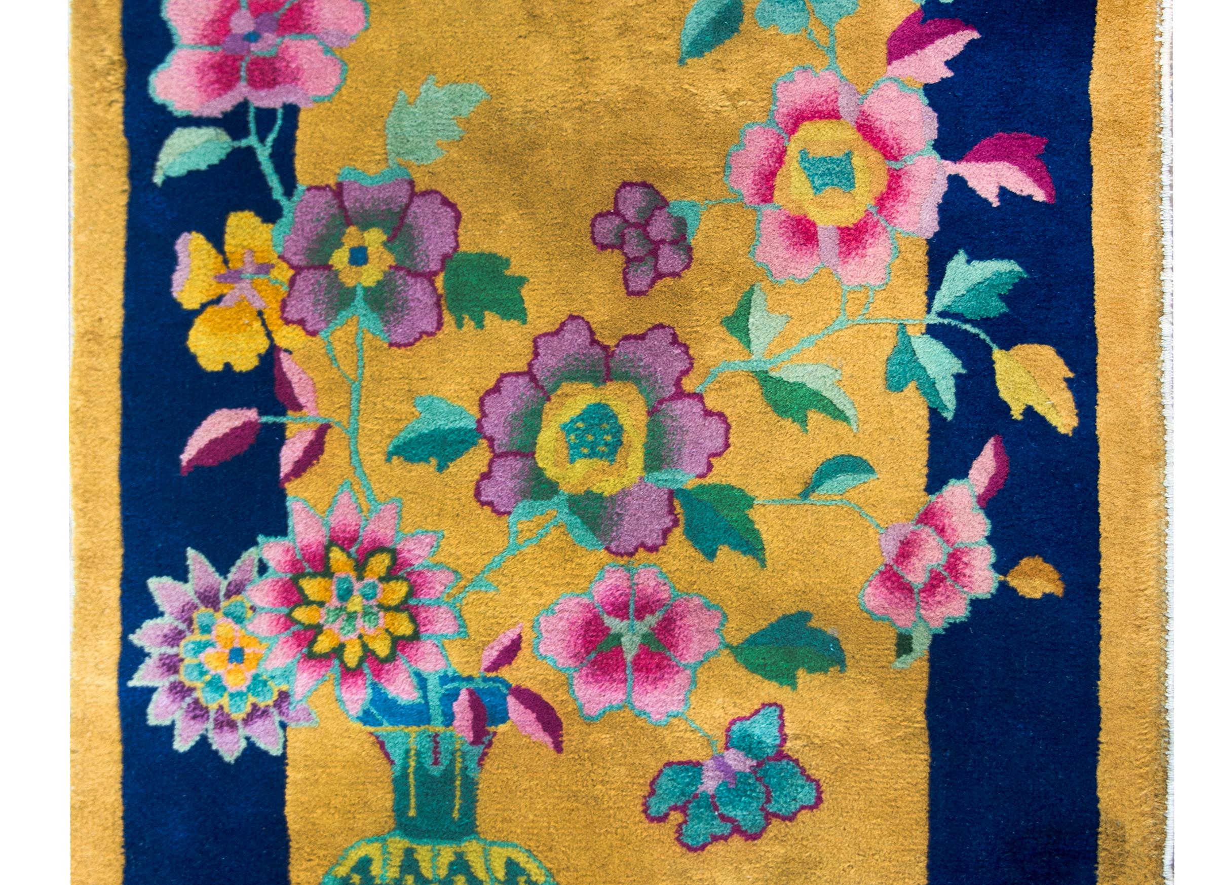 A sweet early 20th century Chinese Art Deco rug with a large vase in one corner, potted with multi-colored peonies, chrystanthemums, and cherry blossoms, and all set against a gold background with a wide indigo striped border.