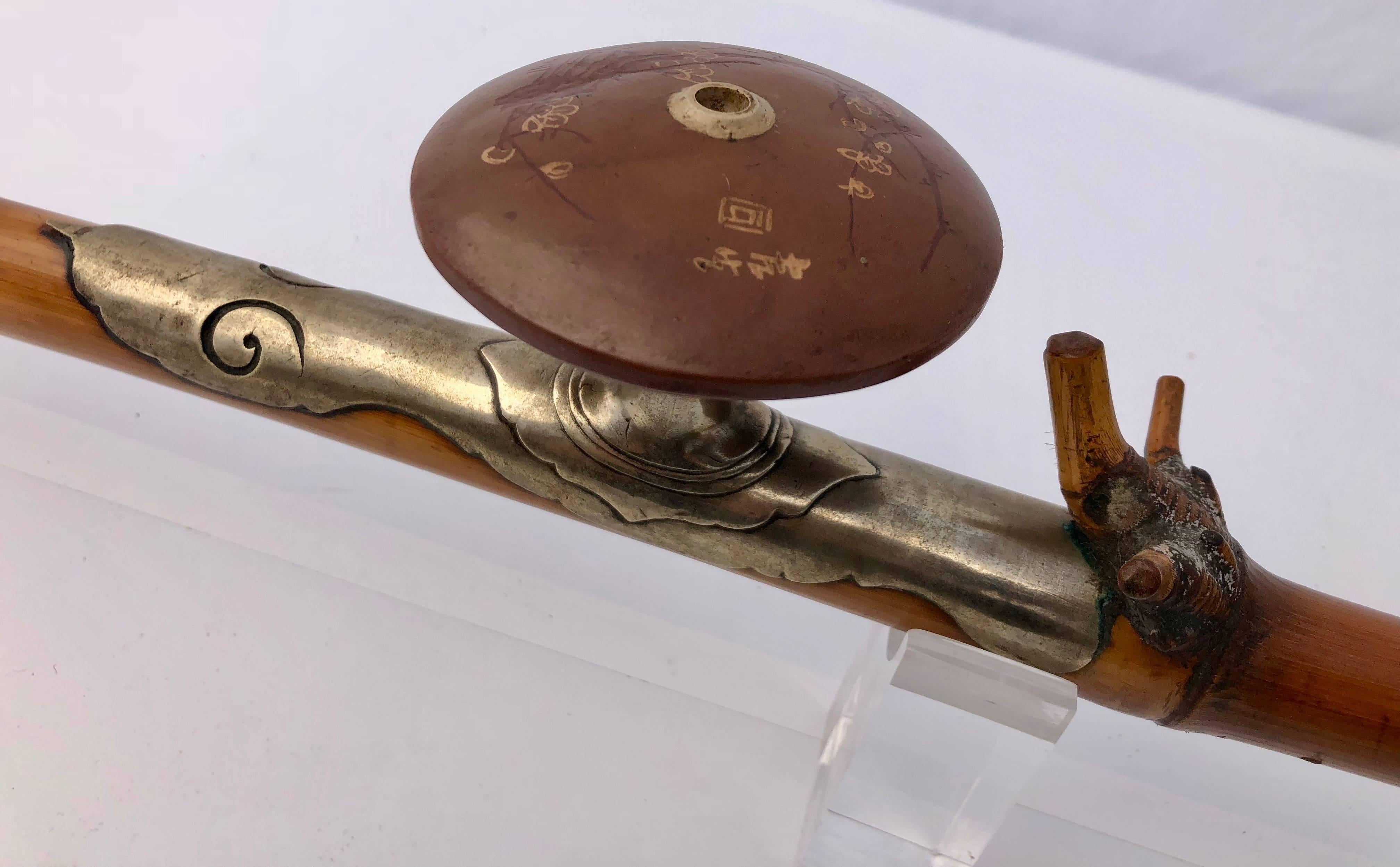 This early 19th century Chinese opium pipe has a bamboo body and silver saddle with a jade mouthpiece and cap. The yixing bowl is inscribed in Chinese and decorated with lotus flowers. 

The lotus is considered divine and one of nature's mystical