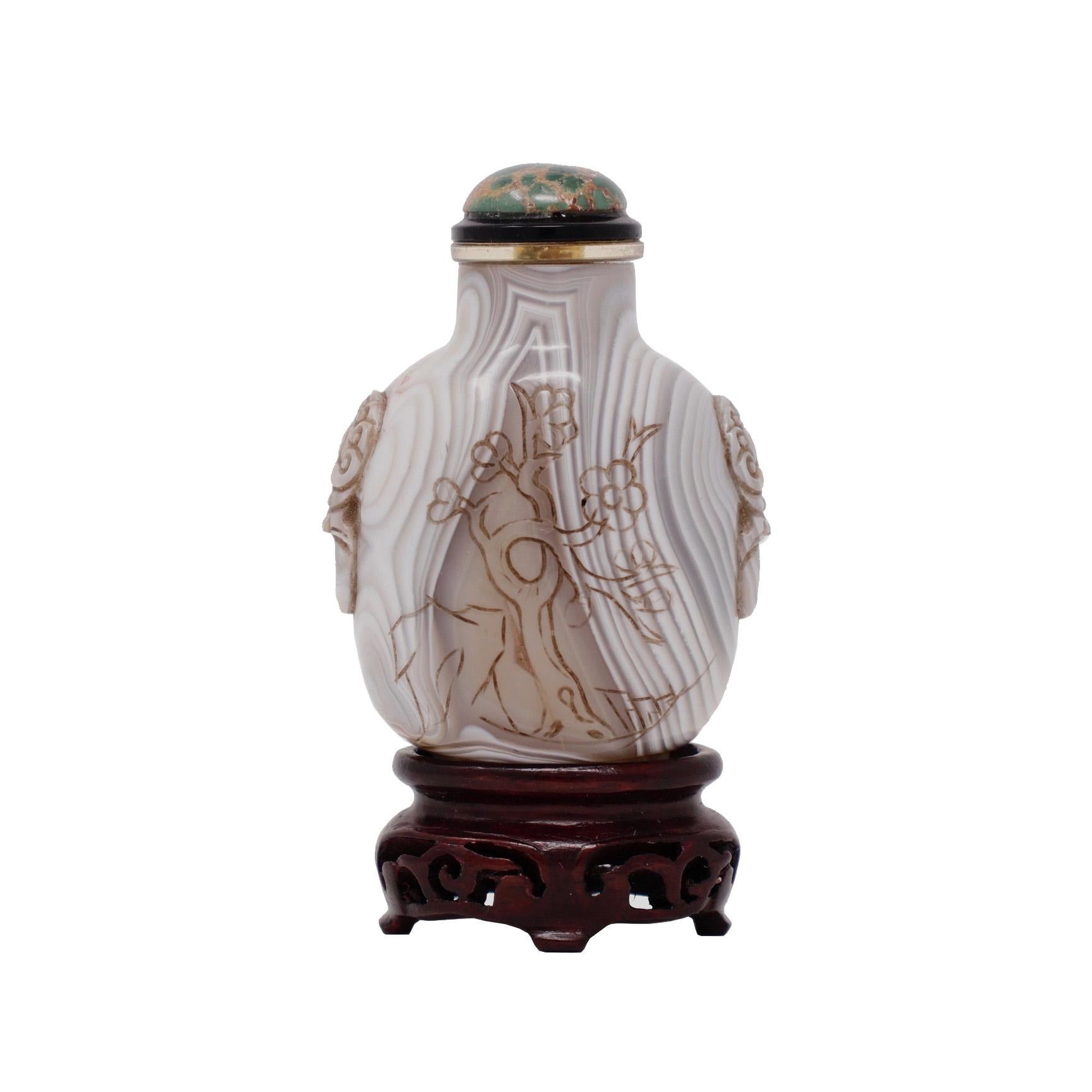 Chinese banded agate snuff bottle of flattened ovoid form, carved with a mock lion mask and ring handle on each shoulder, sturdy raised oval foot, countersunk base, flat mouth rim and narrow aperture, one side with symmetrical banding the other with