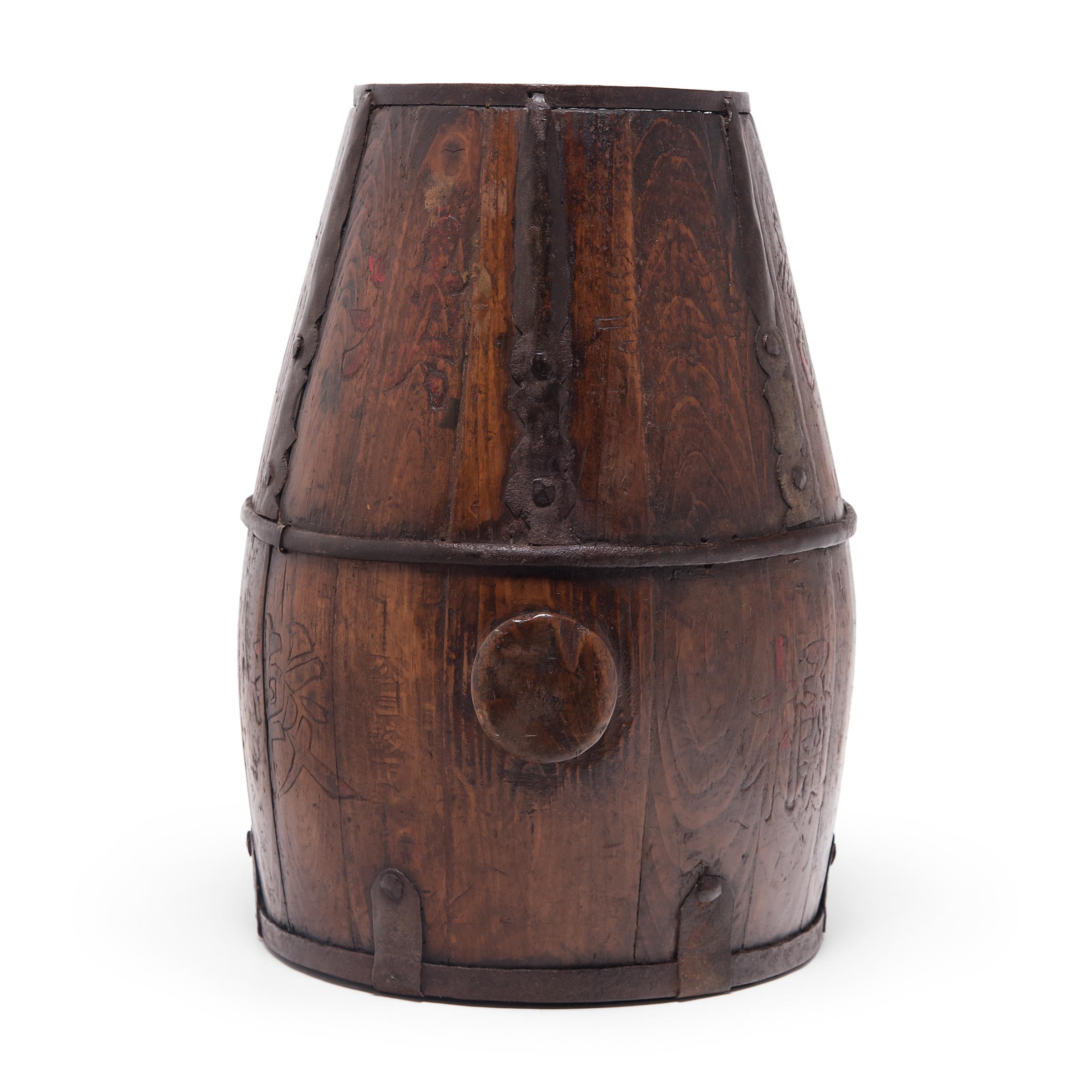 This hand-crafted wood container dates to the early 20th century and was used to store rice and other grains. Darkened by a rich patina, the bucket is elegantly constructed of pinewood staves bound with iron rings and decorative iron fittings. The
