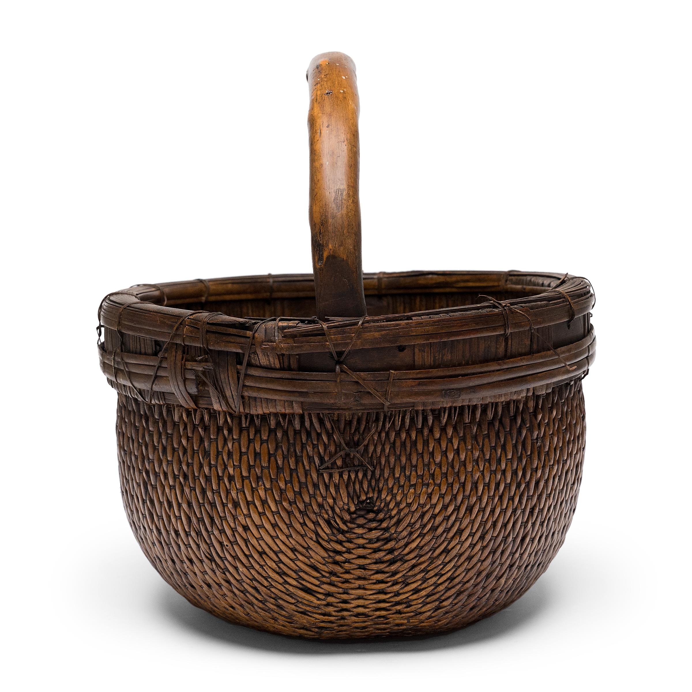 It is easy to imagine someone, long ago, gathering a harvest from their garden or strolling to the market with this beautiful basket tucked under their arm. The round basket has been artfully woven by hand of willow and cord around a bent bamboo