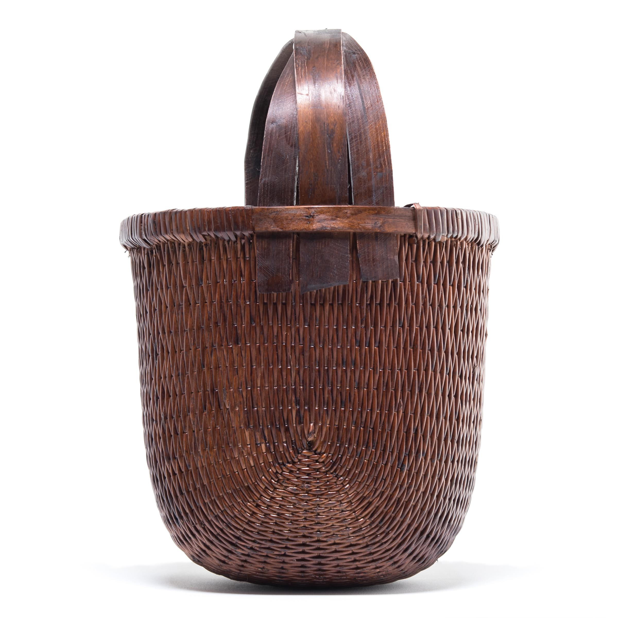 Basket making is an ancient and humble craft, but in the hands of a skilled weaver a simple willow basket can become a truly beautiful work of art. This bent handle basket was made in China long ago, and the artisan’s mastery is evident: the strong,