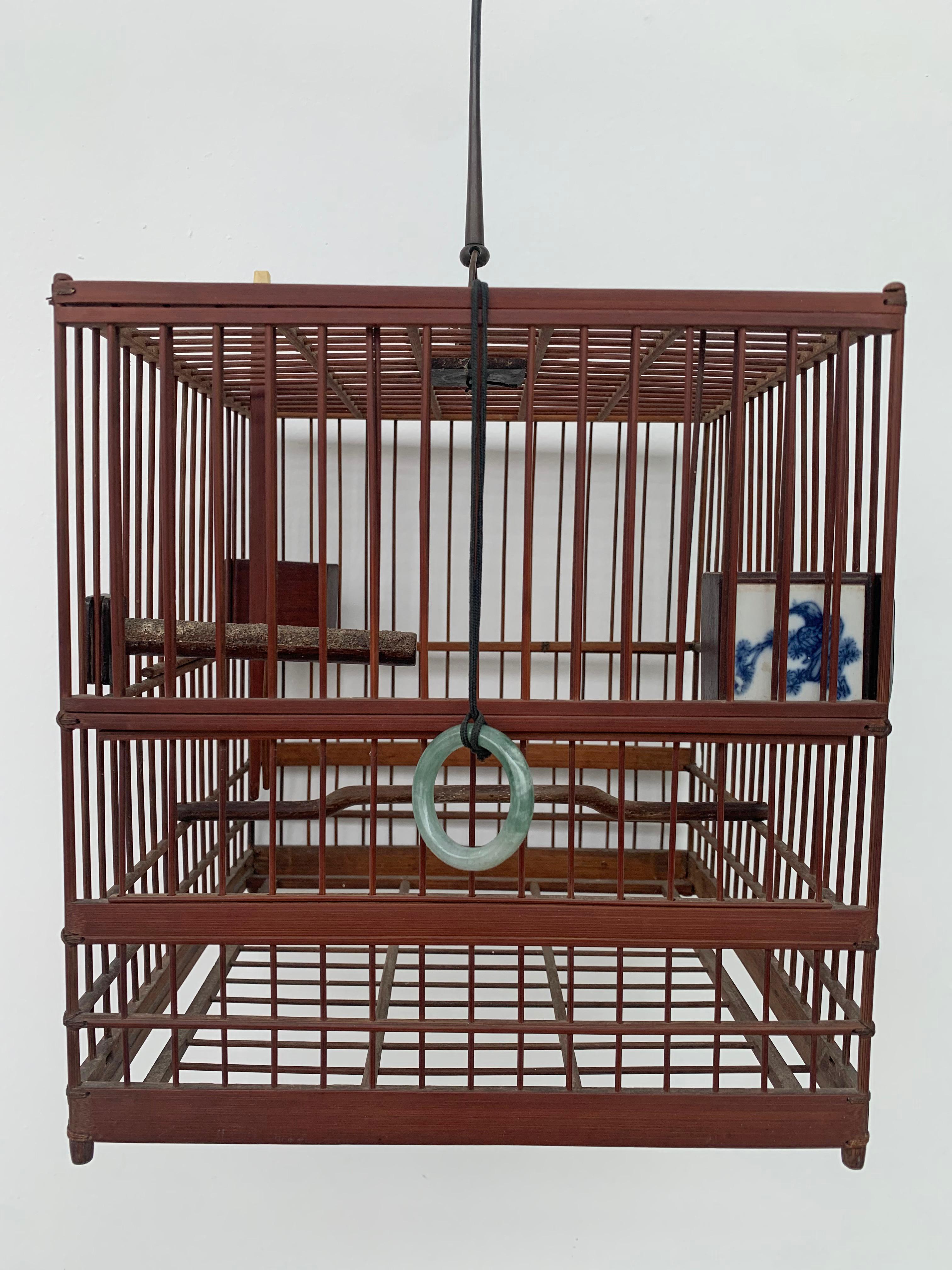 A bamboo birdcage adopting a square shape with a handle for hanging. The cage features 2 porcelain feeding bowls as well as two lifting doors on opposing sides. Overall this cage features beautiful craftsmanship. 

Dimensions: Height 24cm x Width