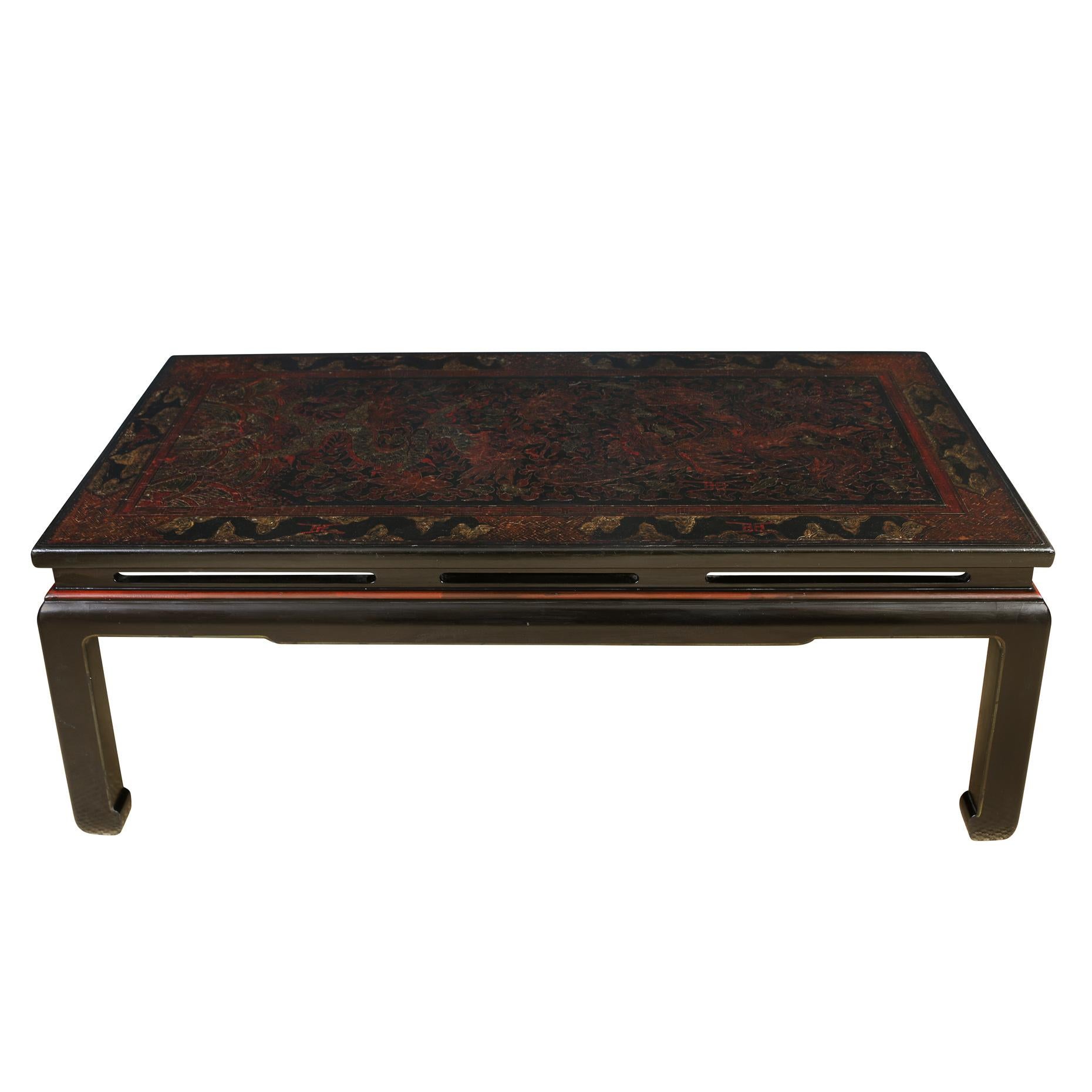 A vintage Chinese black and red lacquer etched coffee table.  The rectangular dark table features a top etched with geometric and floral chinoiserie shapes and phoenix designs with red accents and sits on Ming shaped legs 