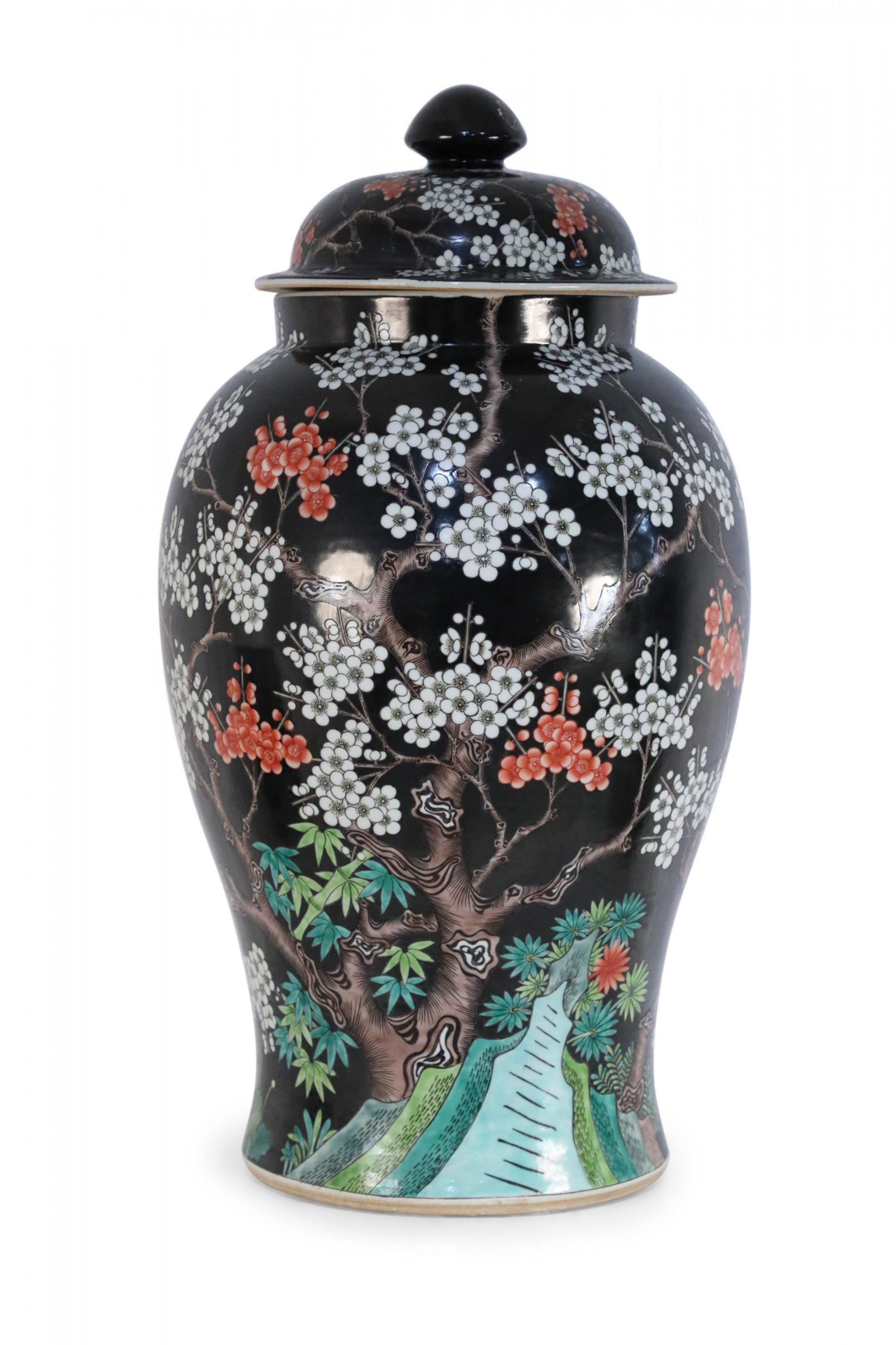 Chinese black porcelain jar with red and white cherry blossom trees growing from a green pastoral scene at the base.
 