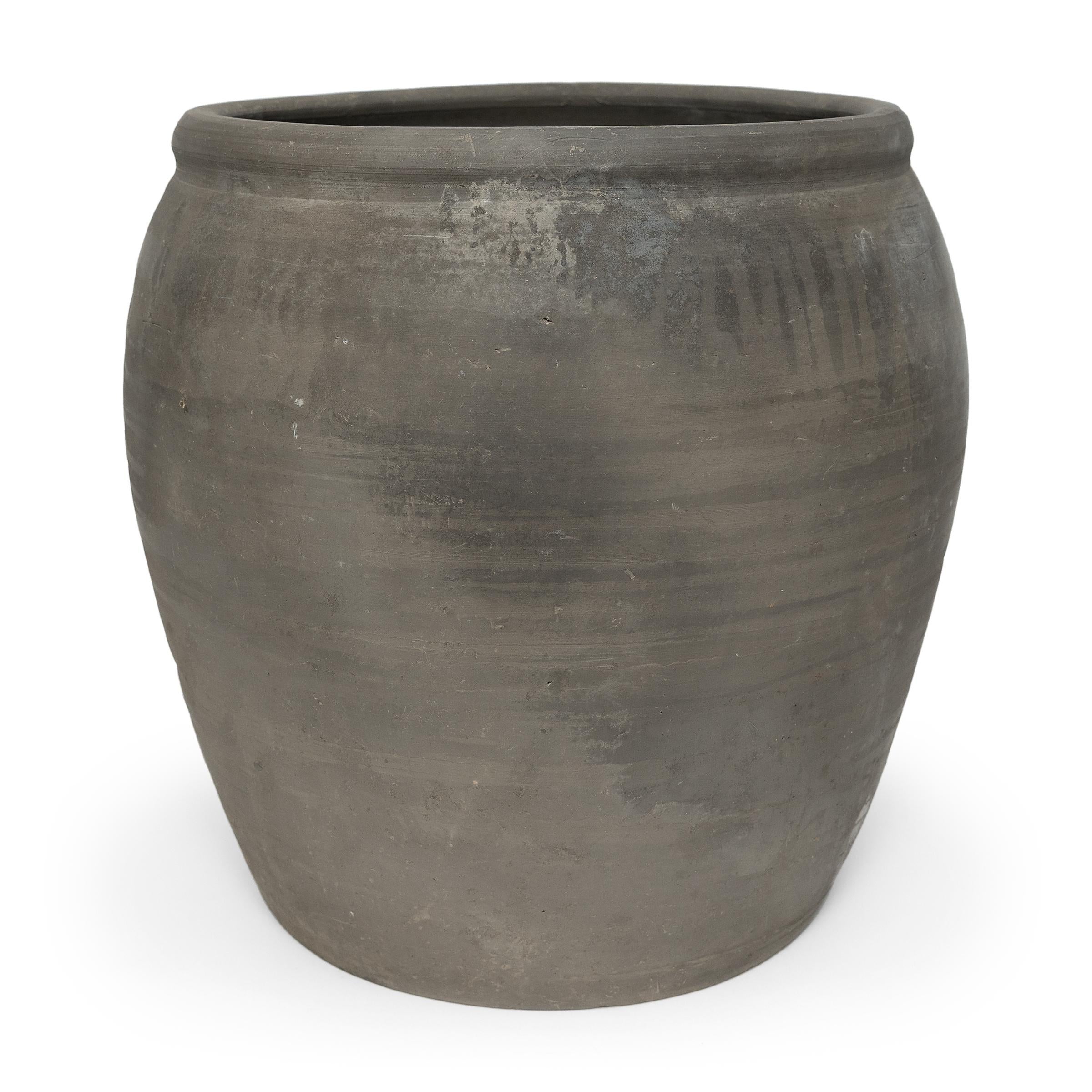 Sculpted during the early 20th century in China's Shanxi province, this vessel has a smoky grey-black exterior with a beautifully irregular unglazed surface. Charged with the humble task of storing dry goods, this tall earthenware jar has a tapered