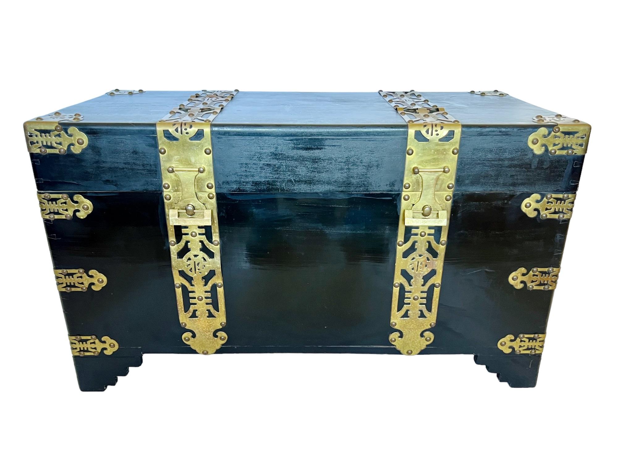 This striking early 20th century Chinese trunk or blanket chest is bound in brass and features a black lacquer finish, dovetail construction, medallion backplate side handles and dual latches with traditional brass locks and a key. It is lined in