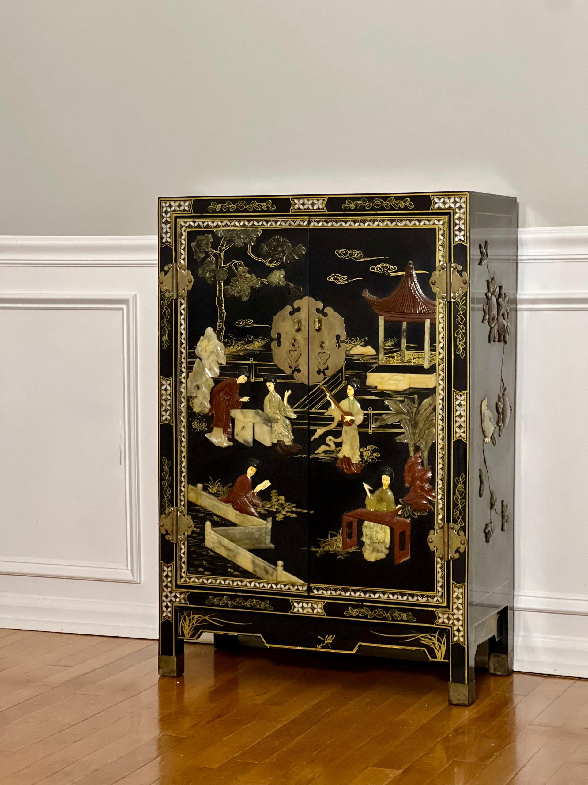 Elegant midcentury Chinese black lacquer two-door cabinet with hardstone and mother-of-pearl inlay.  Carved hardstone in relief throughout depicts a pavilion garden scene with courtly ladies on the front and fruit trees with birds on the sides. 