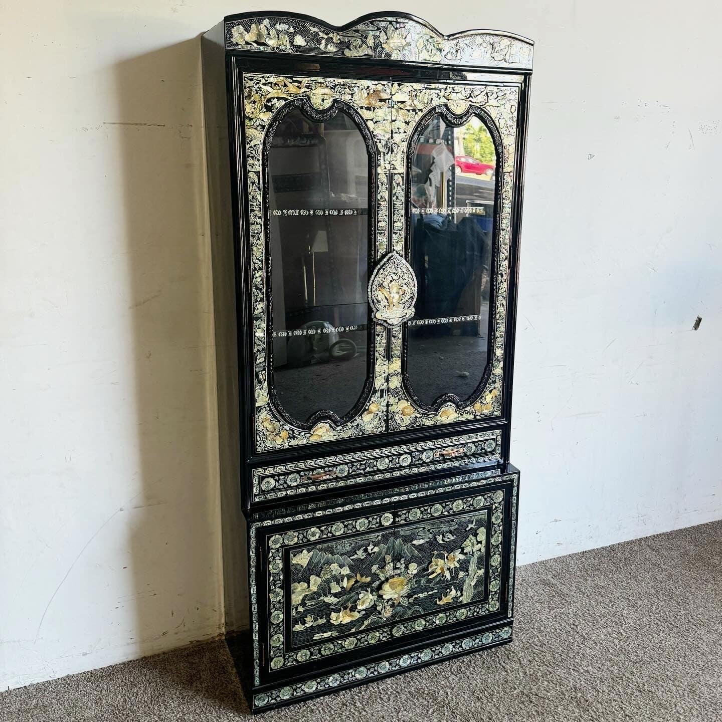 Esta impresionante vitrina china lacada tiene madera lacada en negro con intrincadas incrustaciones de nácar. Los diseños detallados y el exclusivo tirador en forma de mono realzan su belleza, mientras que las puertas con frente de cristal y los