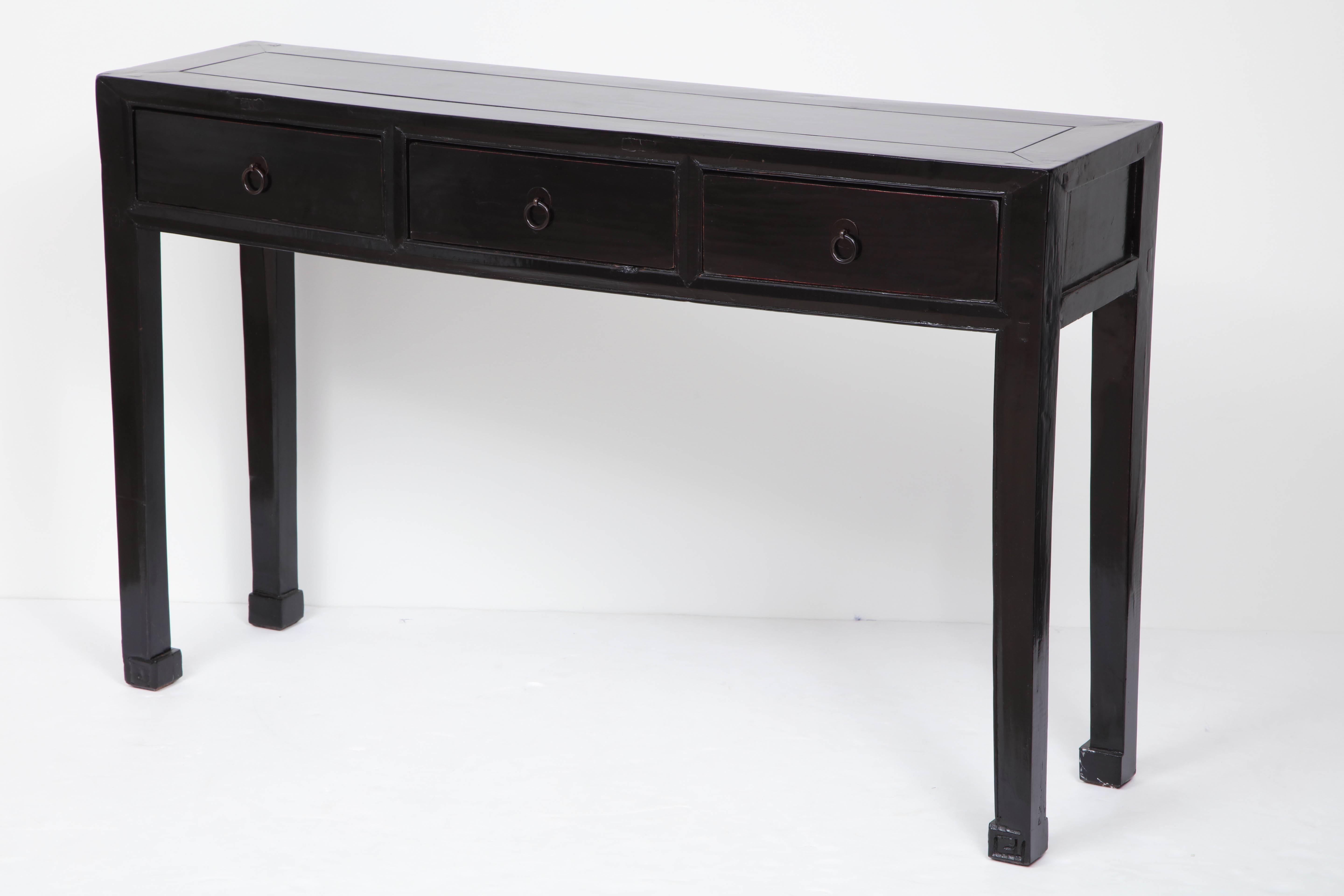 A Chinese black lacquered console, circa 1920s, with a rectangular paneled top above three frieze drawers raised on square legs with key carved feet.