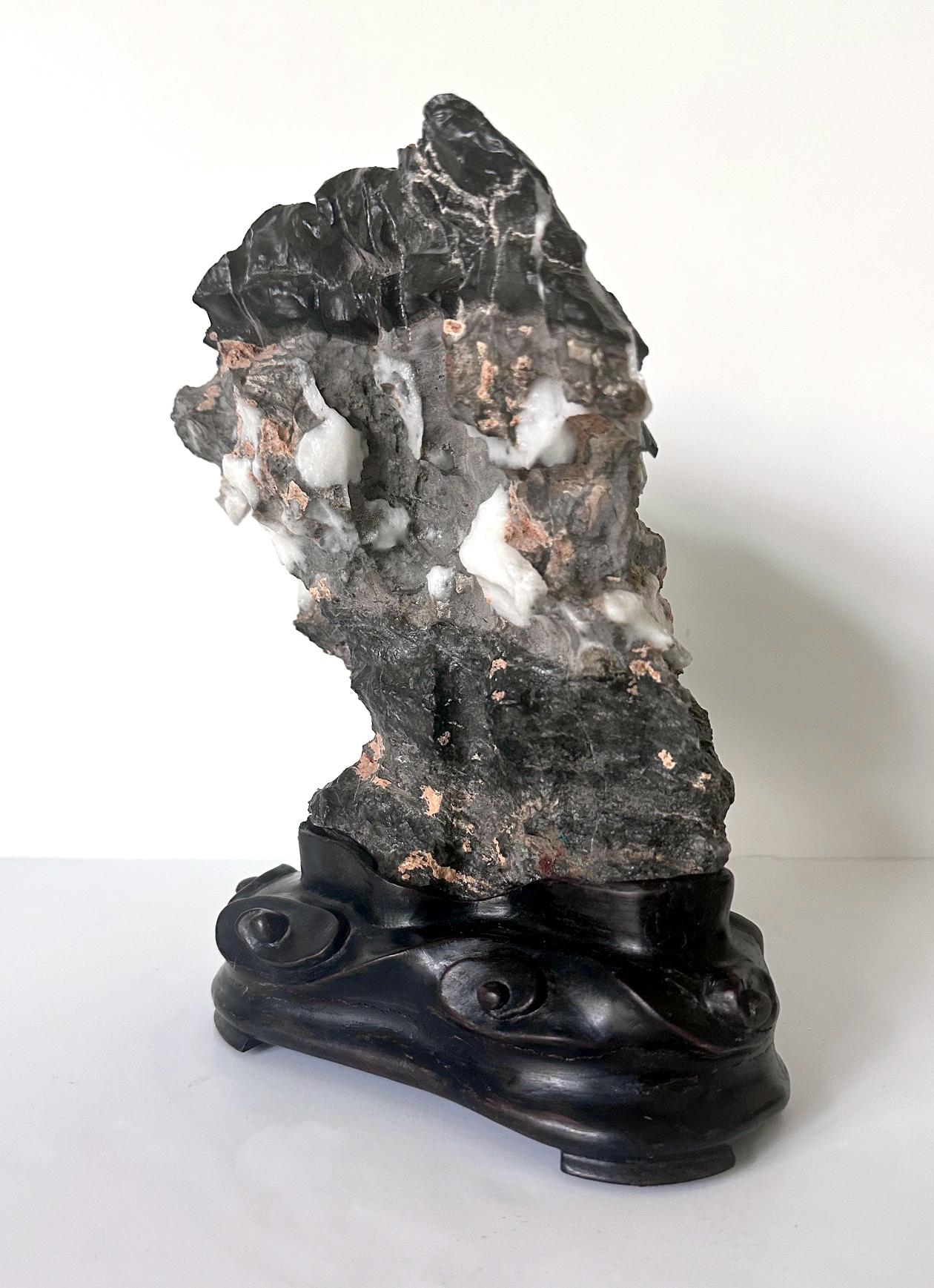 A Chinese scholar stone of white Lingbi type in upright mushroom form presented on a carved conforming wood base. The type of special Lingbi known to the collector as white Lingbi features scattered white deposits of crystalized silica and calcium