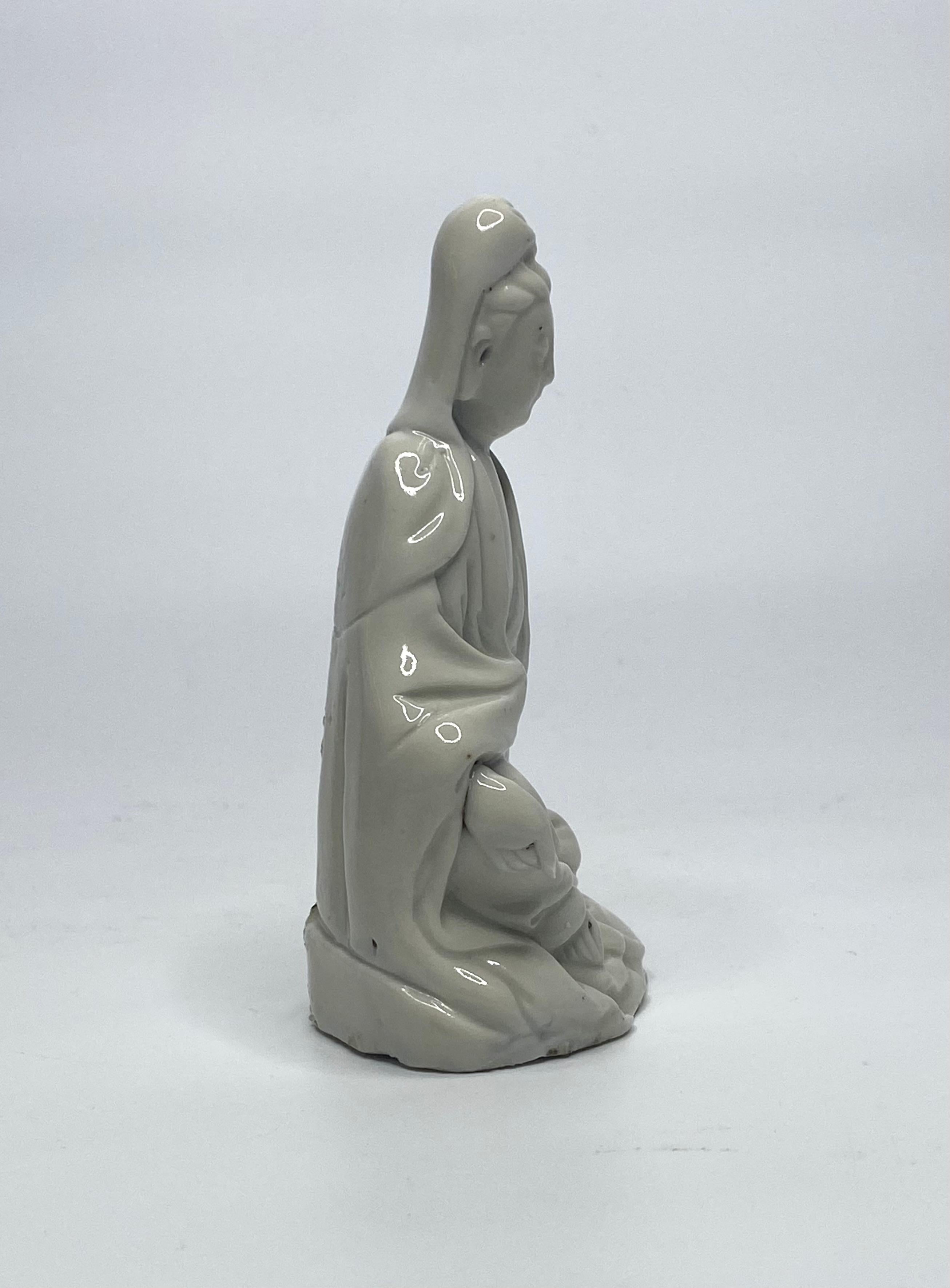 Chinese blanc de chine figure of Guanyin, Dehua, late 17th Century. The goddess, modelled seated, wearing flowing robes, revealing her right hand, and foot. Her head is covered by a cowl. The whole covered in a blanc de chine glaze.
Height – 12 cm,