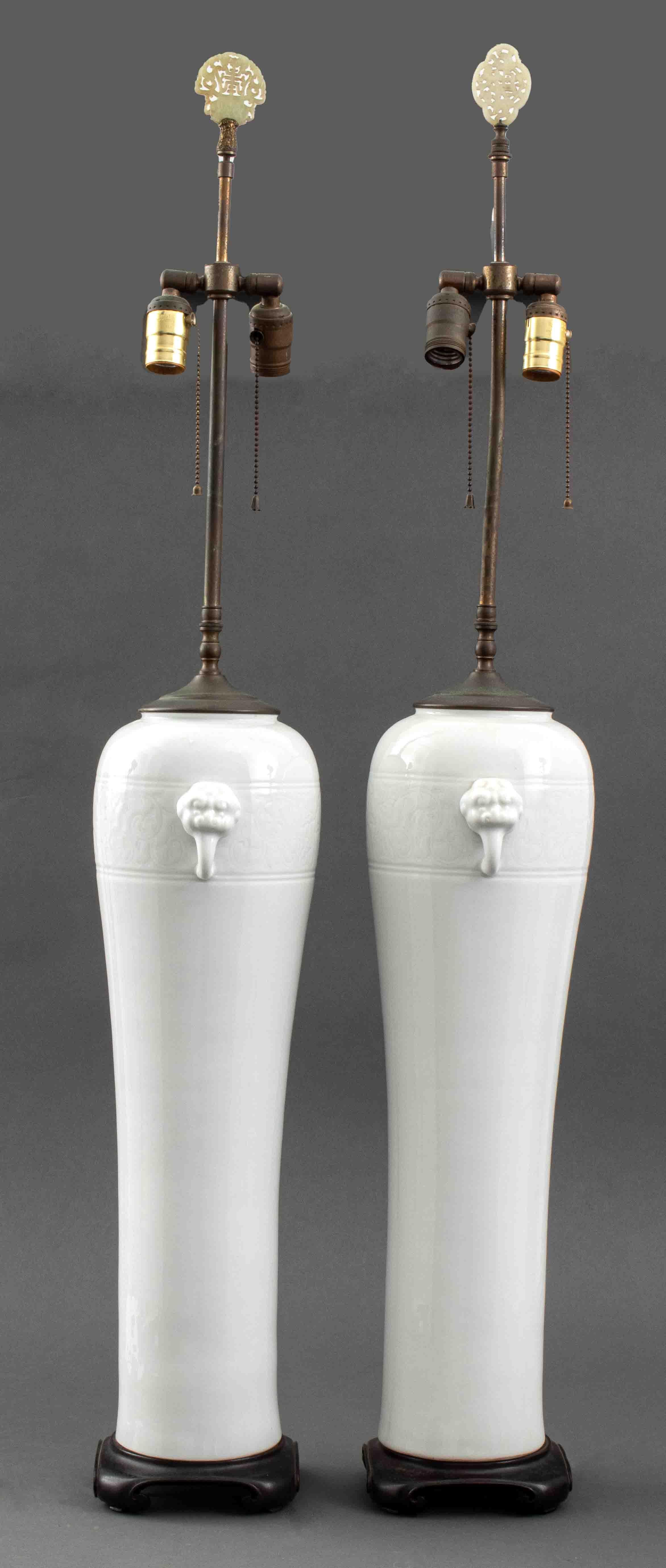 Pair of Chinese blanc de Chine ceramic pottery porcelain elongated plum vases with two animal figural handles and scrolling foliate border, mounted upon zitan bases with four scroll feet and fitted as lamps with two bulb sockets, topped with carved