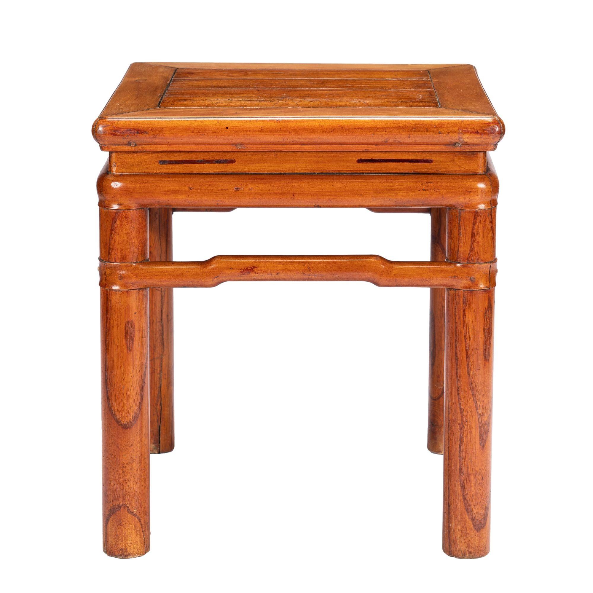 Chinese Yumu wood (Northern Chinese elm) stool in the Ming taste. The waisted and bull nose frame and panel top is engaged to the rounded framing elements including the leg posts. The legs are joined under the table frame with a continuous camel