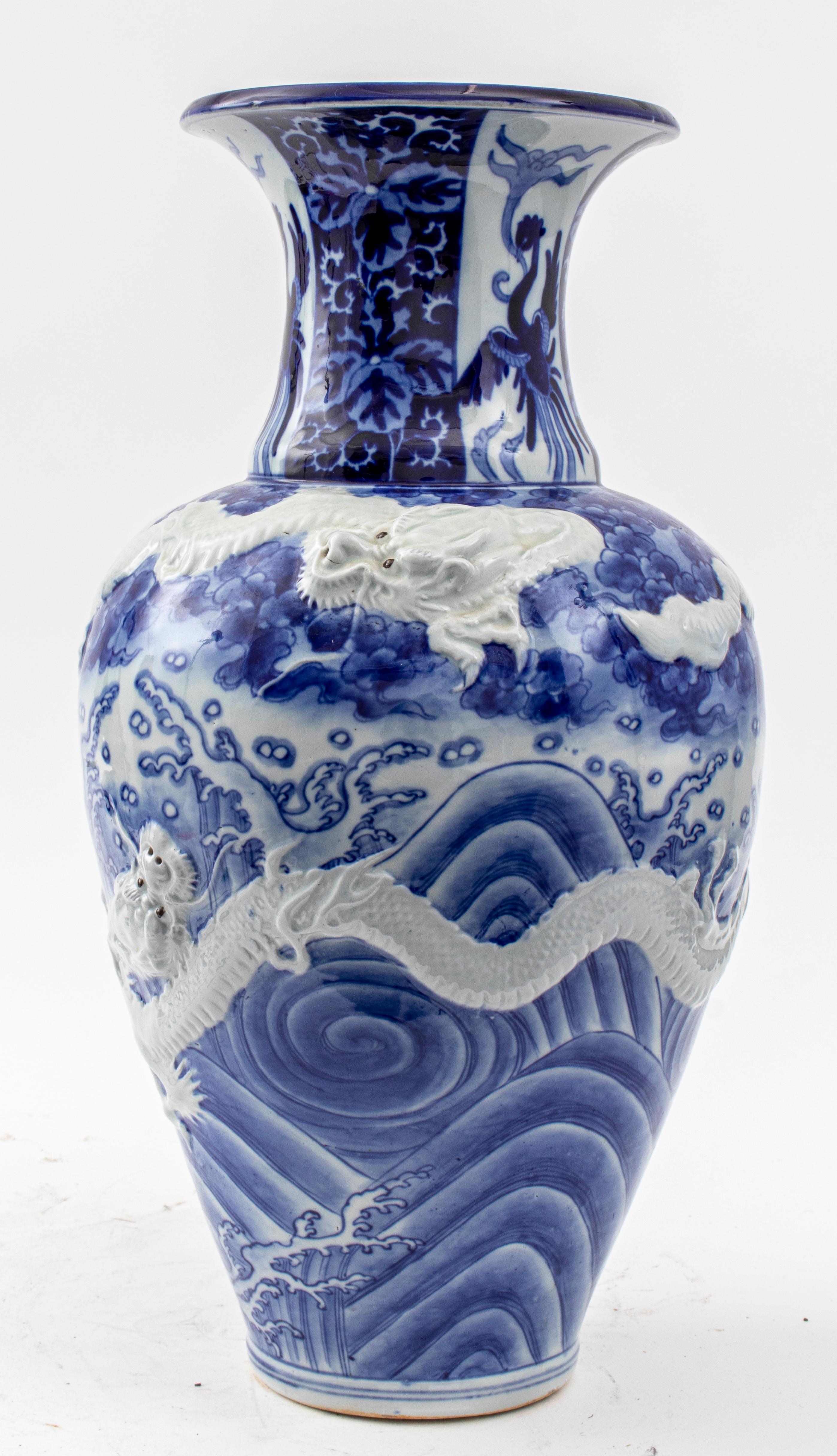 Large Chinese blue and white glazed ceramic pottery porcelain vase of begonia form decorated with two dragons in high relief amongst waves and clouds encircling the body and the neck painted with three phoenixes, scrolling foliate design upon the