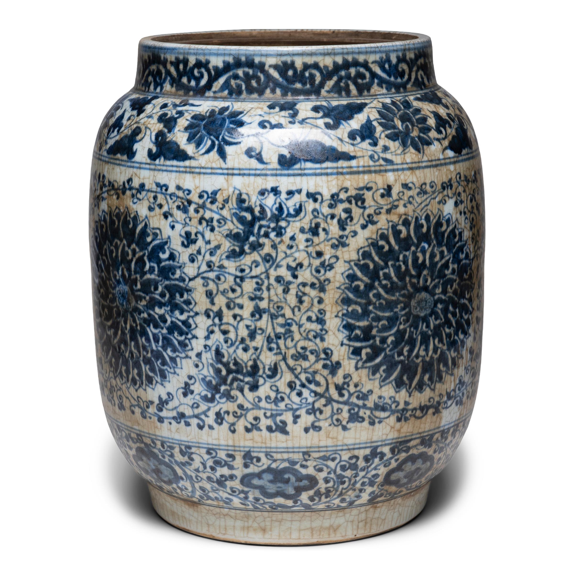 This large drum-form jar continues a centuries-old tradition of Chinese blue-and-white porcelain ware. Hand-painted with cobalt-blue glaze, the jar is festooned with trailing vines and flower blossoms, densely patterned around large chrysanthemum
