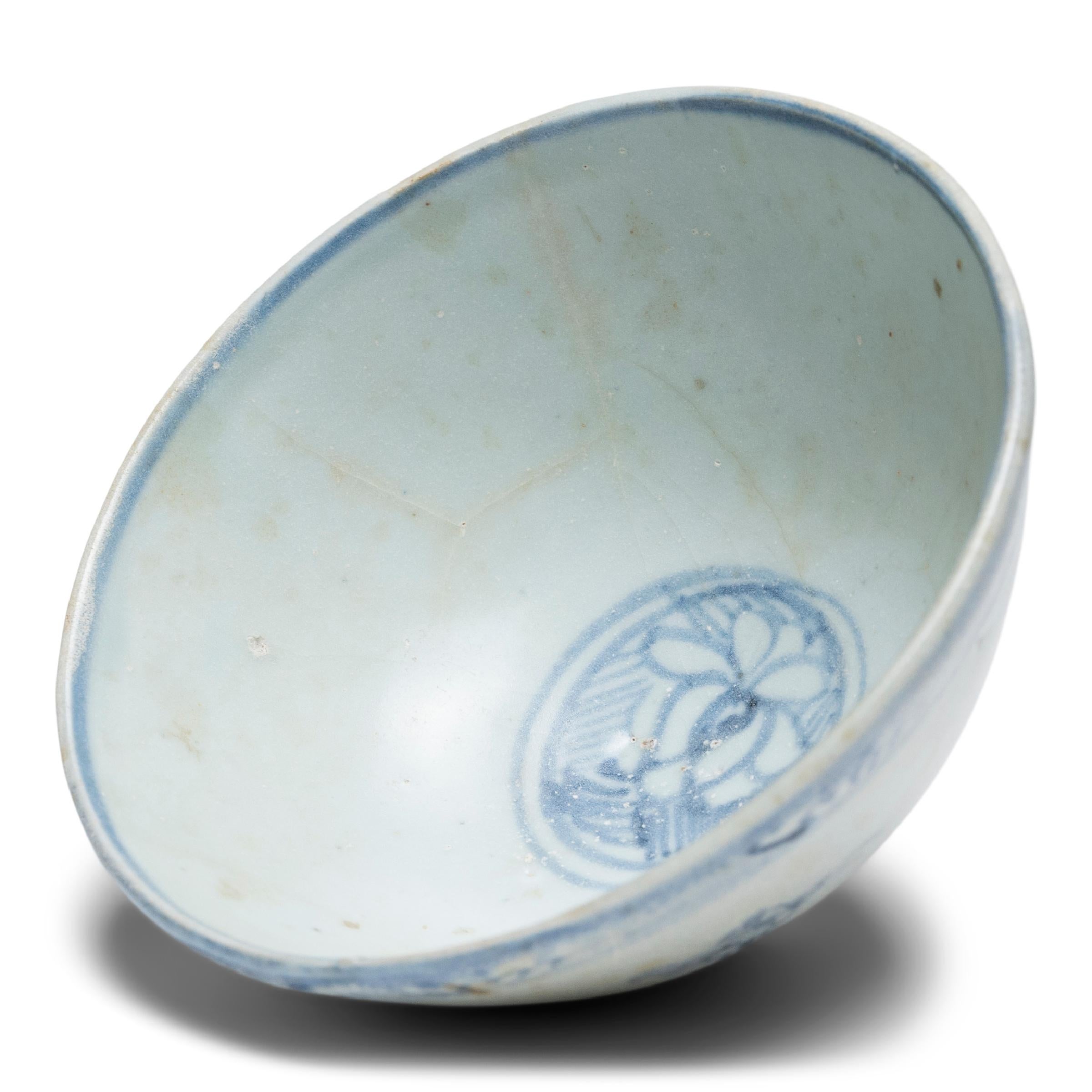 This refined porcelain rice bowl dates to the late Ming dynasty and is beautifully decorated in the blue-and-white style. Expressive sweeps of blue bring the bowl’s simple form to life, adorning its speckled grey-white underglaze with floral motifs