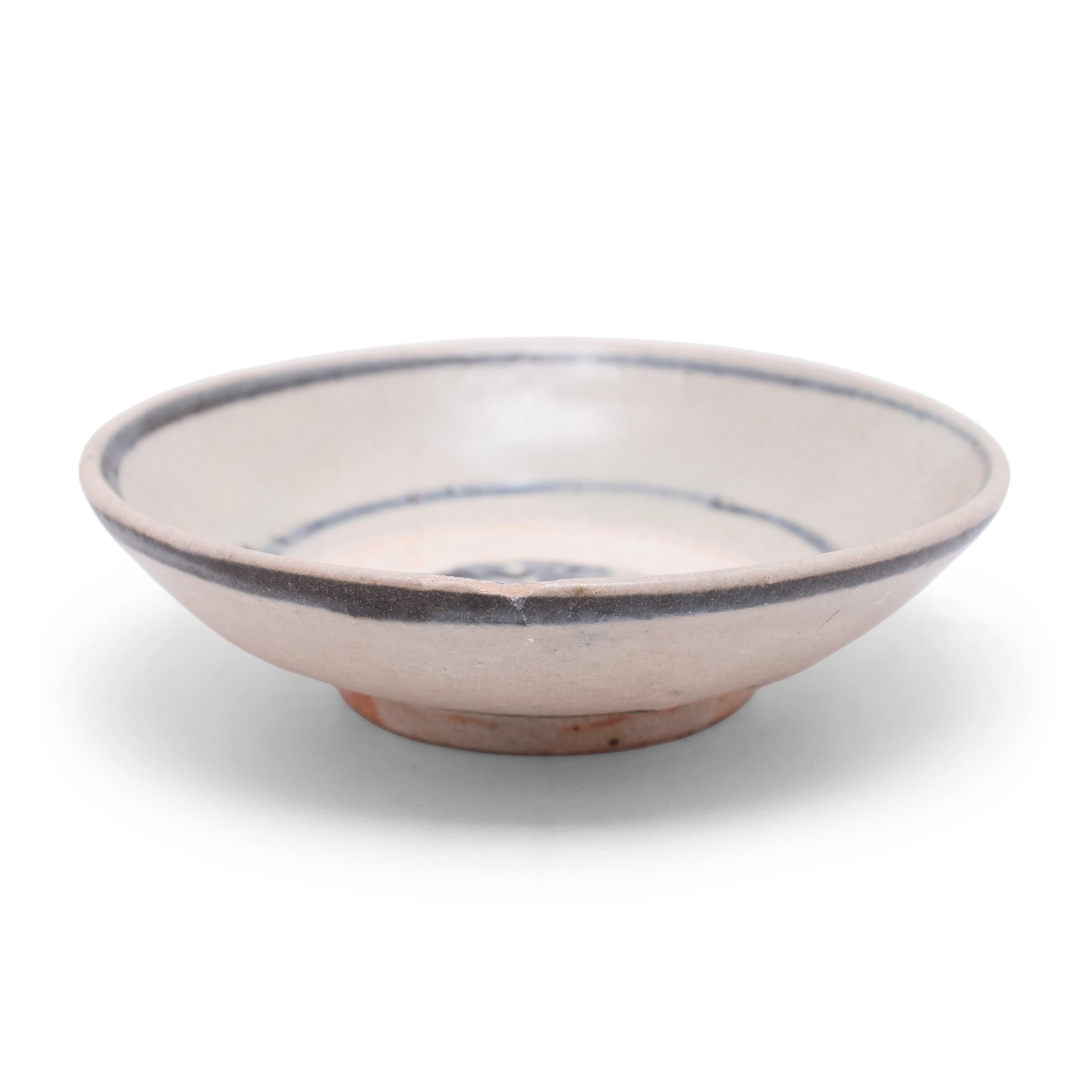 An everyday example of Chinese blue-and-white ceramics, this petite footed dish charms with simple blue brushwork atop a crazed blue-grey underglaze. Bands of blue glaze encircle the lip and frame a loosely brushed chrysanthemum blossom, a symbol of