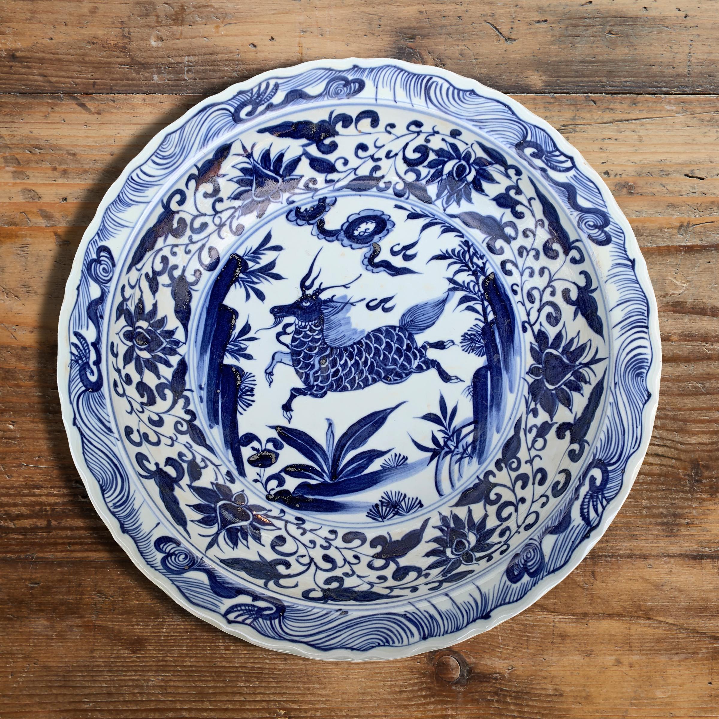 A whimsical large late-20th century Chinese blue and white painted porcelain platter depicting a leaping Qilin, a mythical creature with the body of the dragon, the legs and head of a deer, and the tail of a lion, amidst a landscape of rocks and