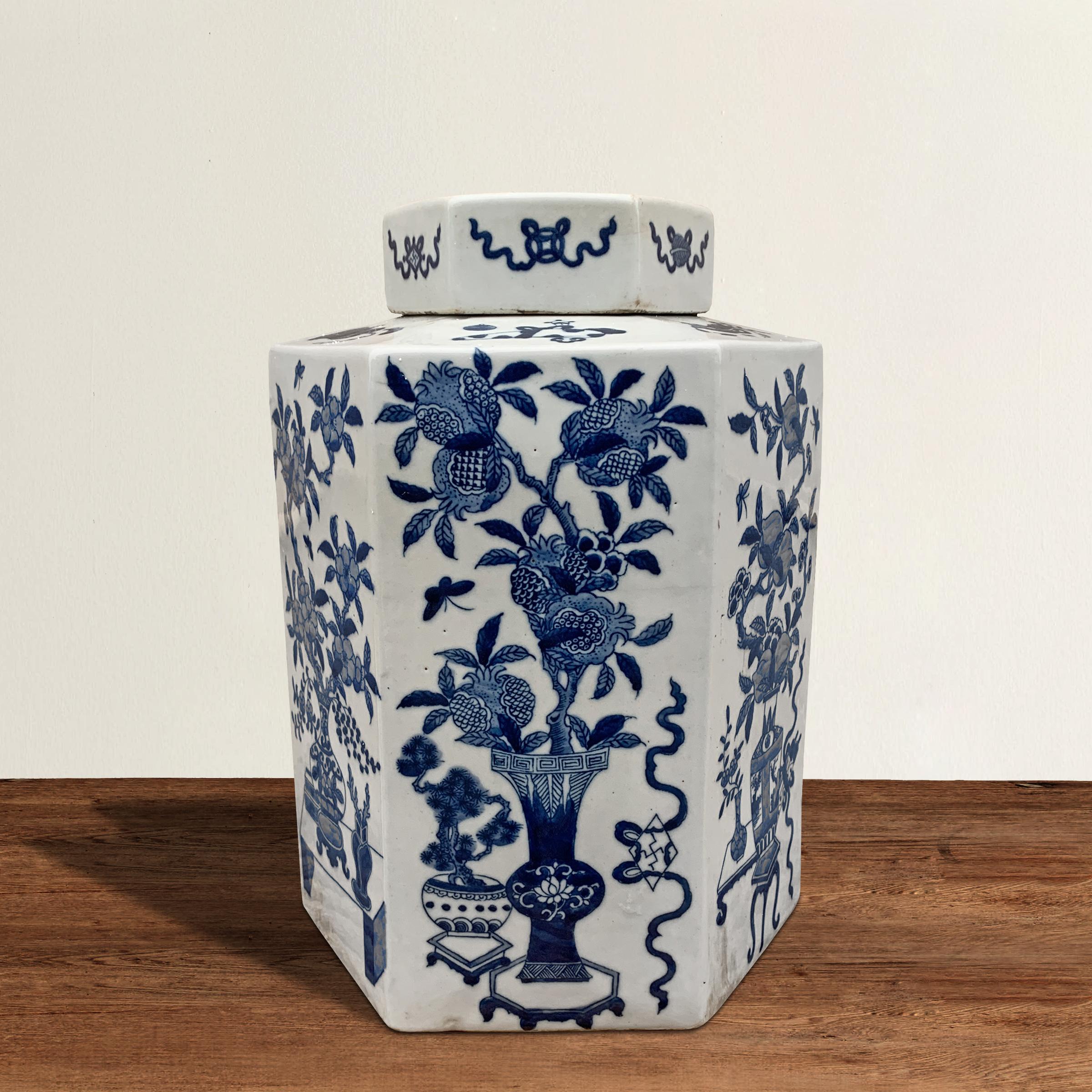 A beautifully blue and white porcelain vase of hexagonal form with a lid, and hand painted with pomegranate, prunes, and peach branches, each potted in vases and surrounded by other auspicious Chinese scholar's objects.